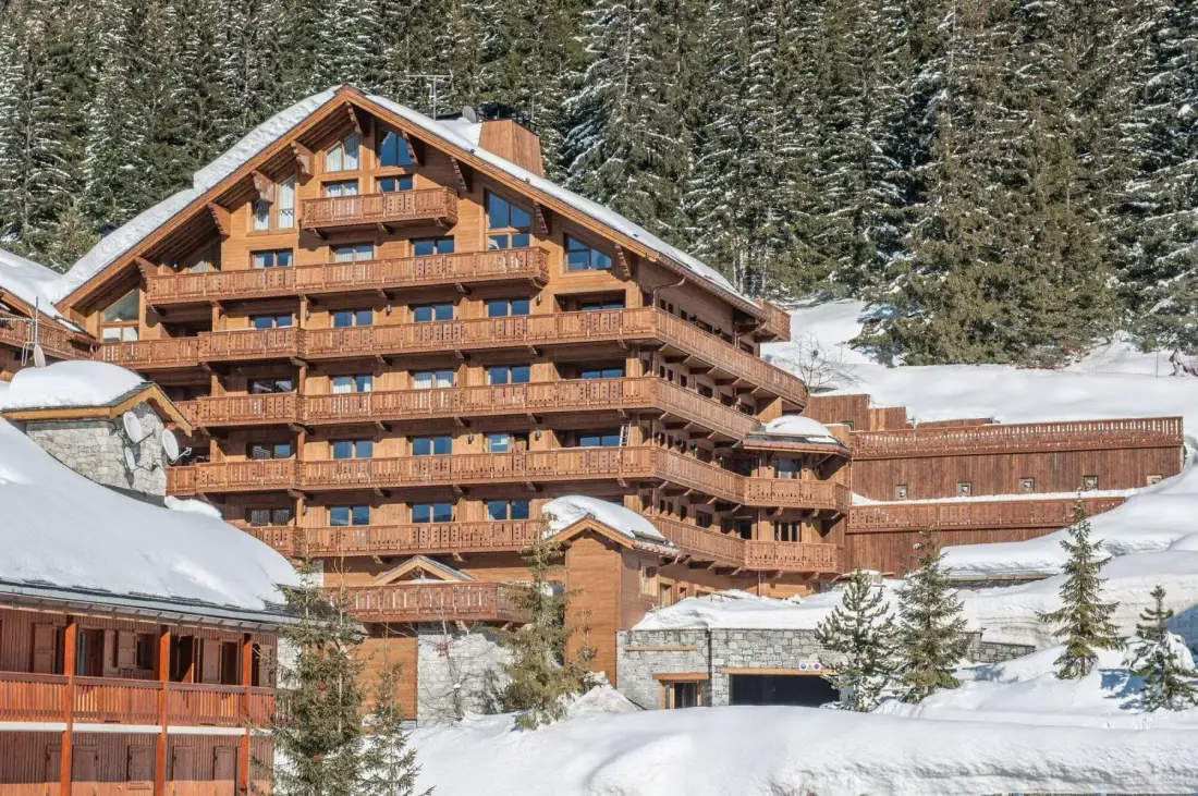 A large wooden chalet stands among snow-covered trees on a mountain slope.