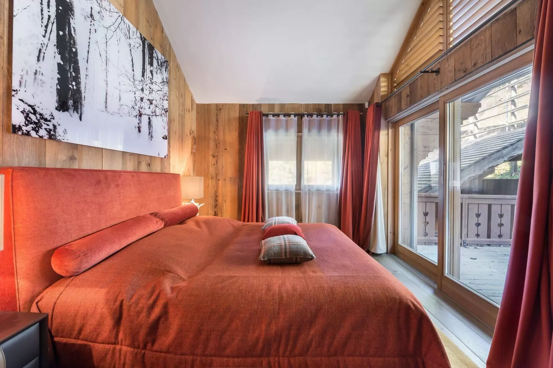 A bedroom with a large bed and windows opening onto a balcony.