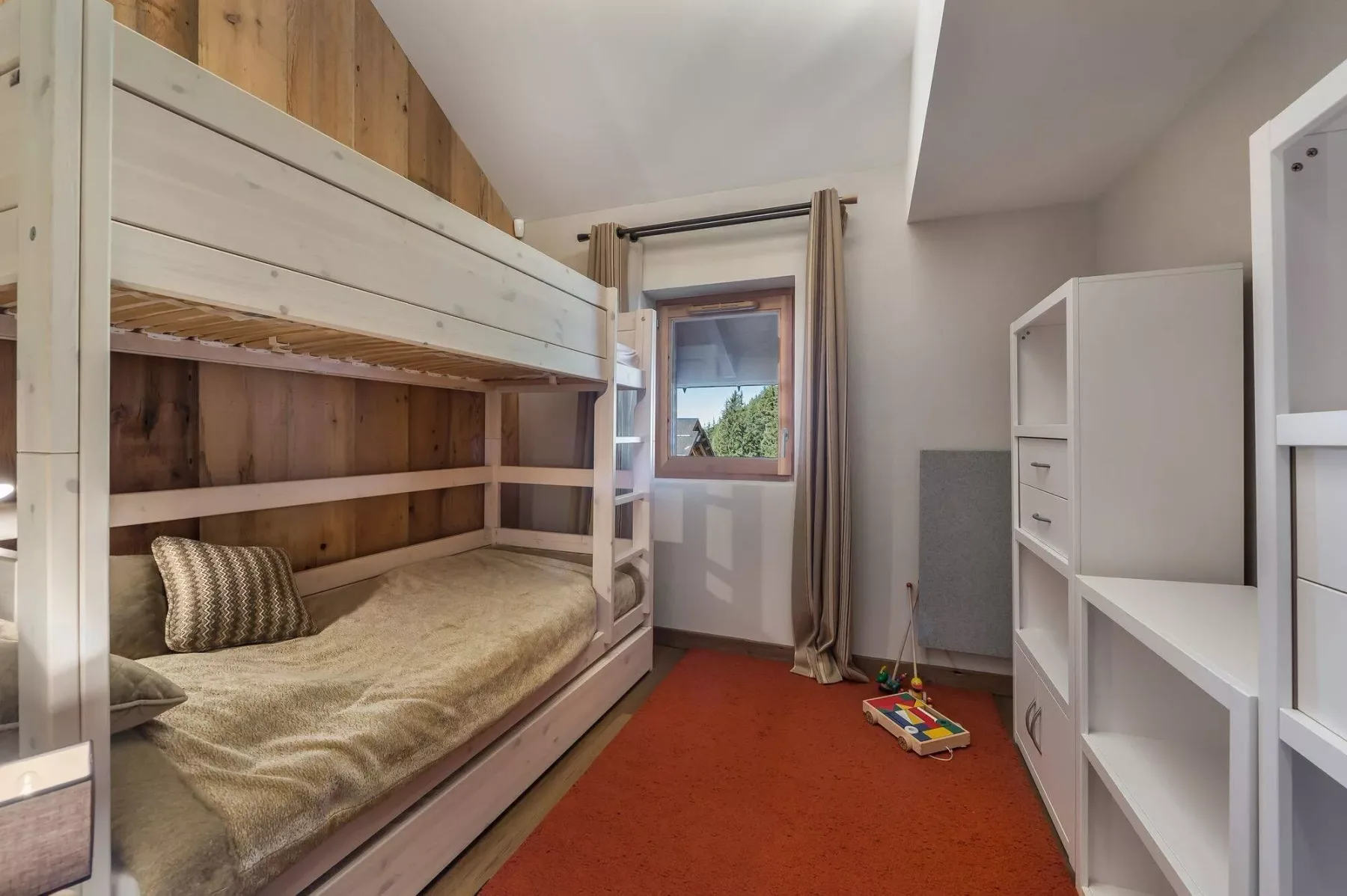A bedroom with a wooden bunk bed, a window, and white shelving.