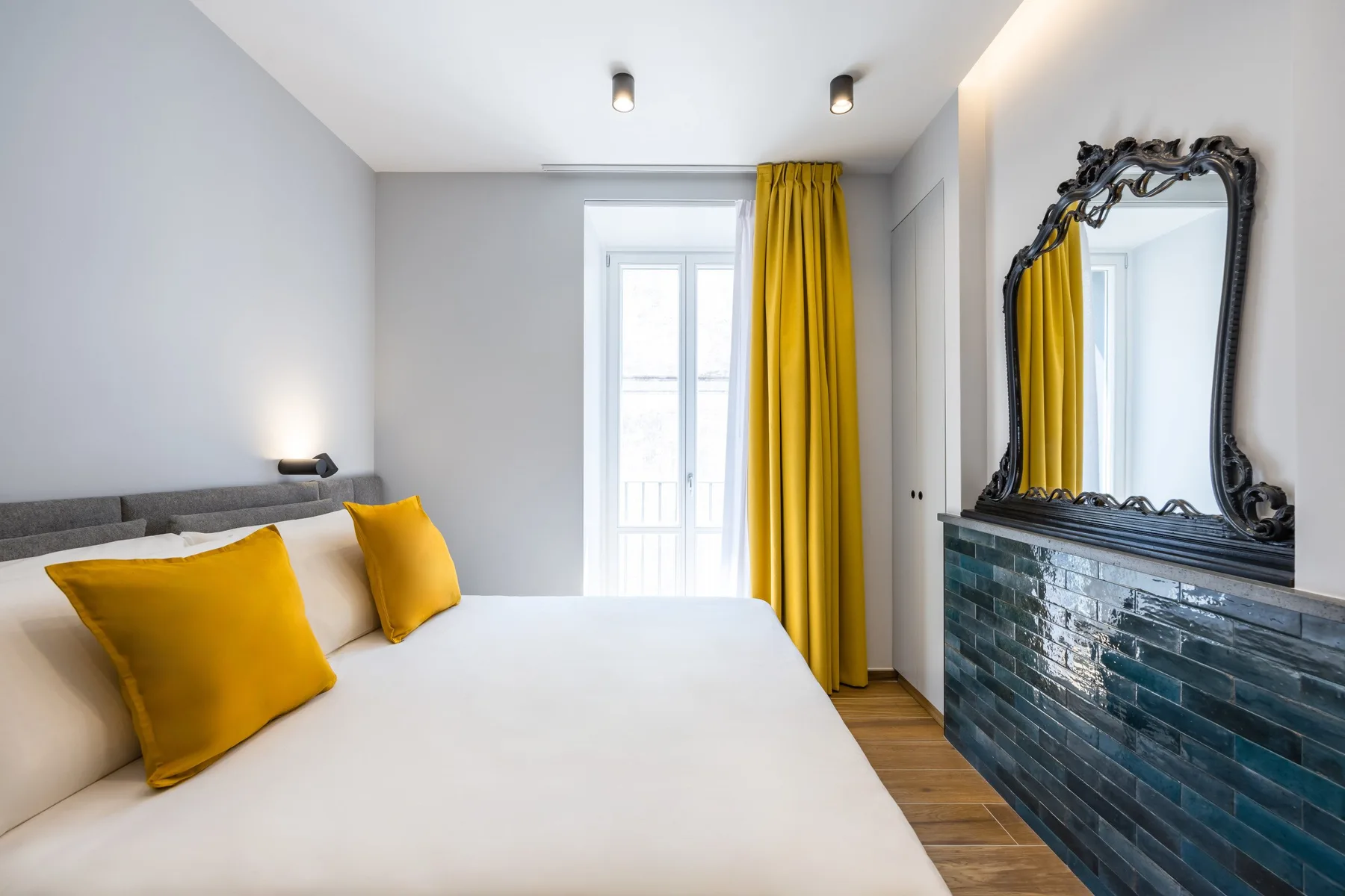 A bright bedroom has a white bed, mustard-yellow curtains, and a decorative mirror.