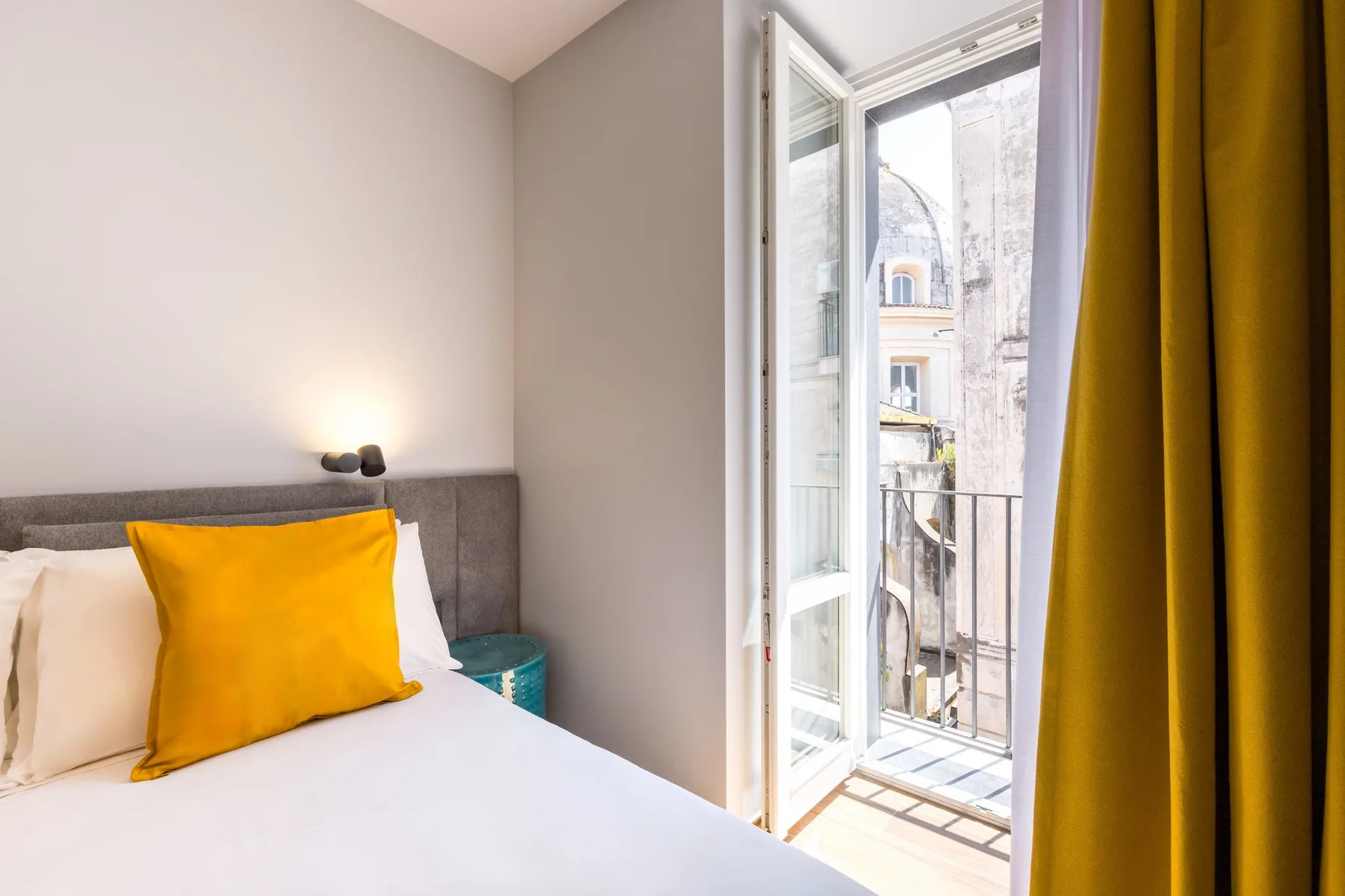 A bedroom with a bed beside an open glass door and yellow curtains.
