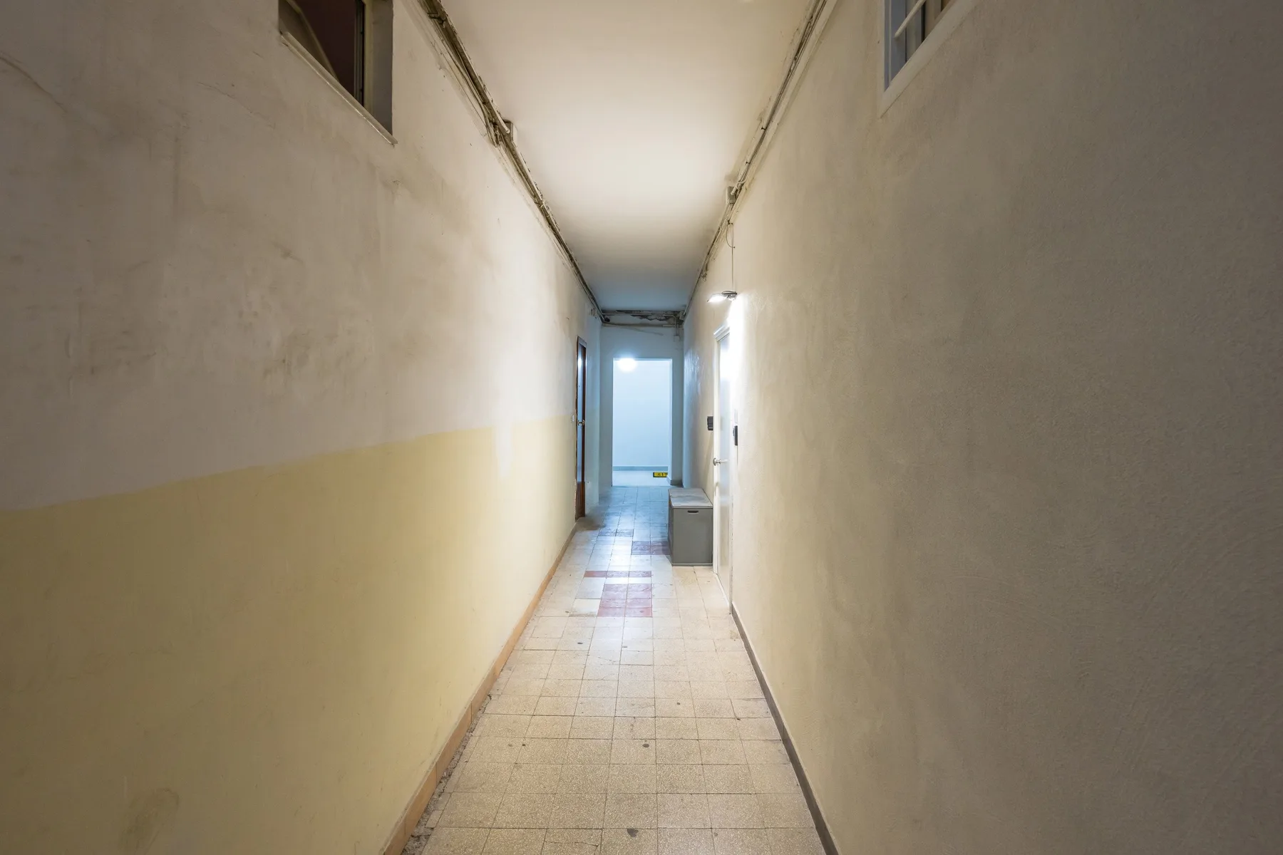 A narrow hallway with tiled flooring leads to a bright doorway.