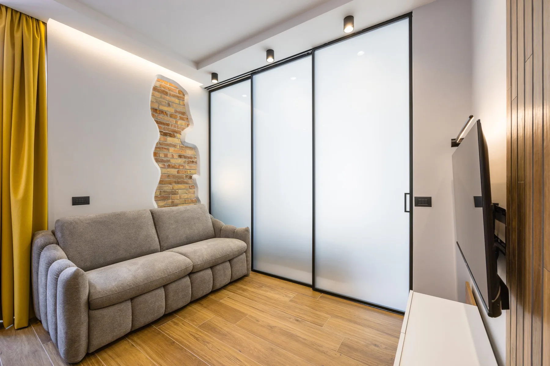 A living room with a gray sofa, frosted glass panels, and wood flooring.