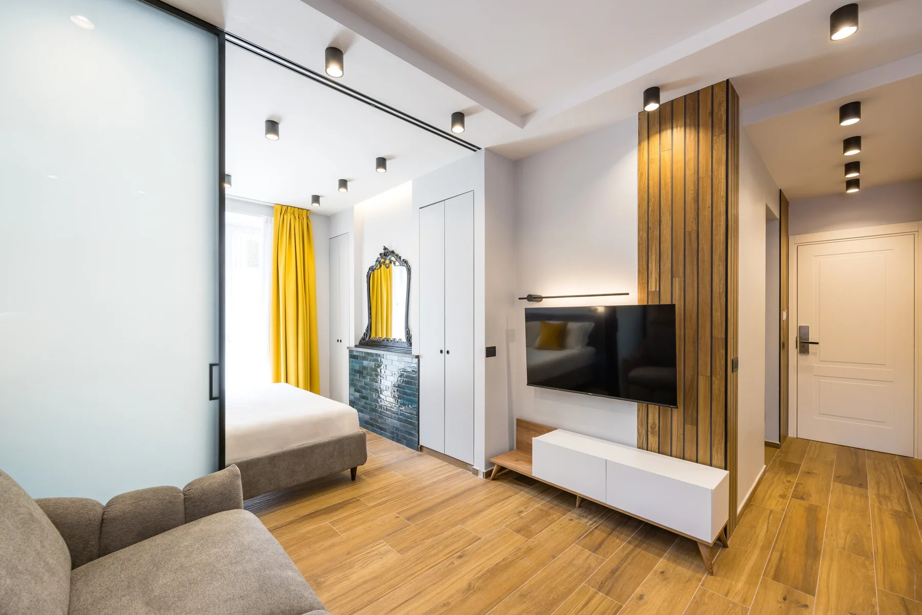 A bedroom and sitting area with a bed, television, and wood flooring.