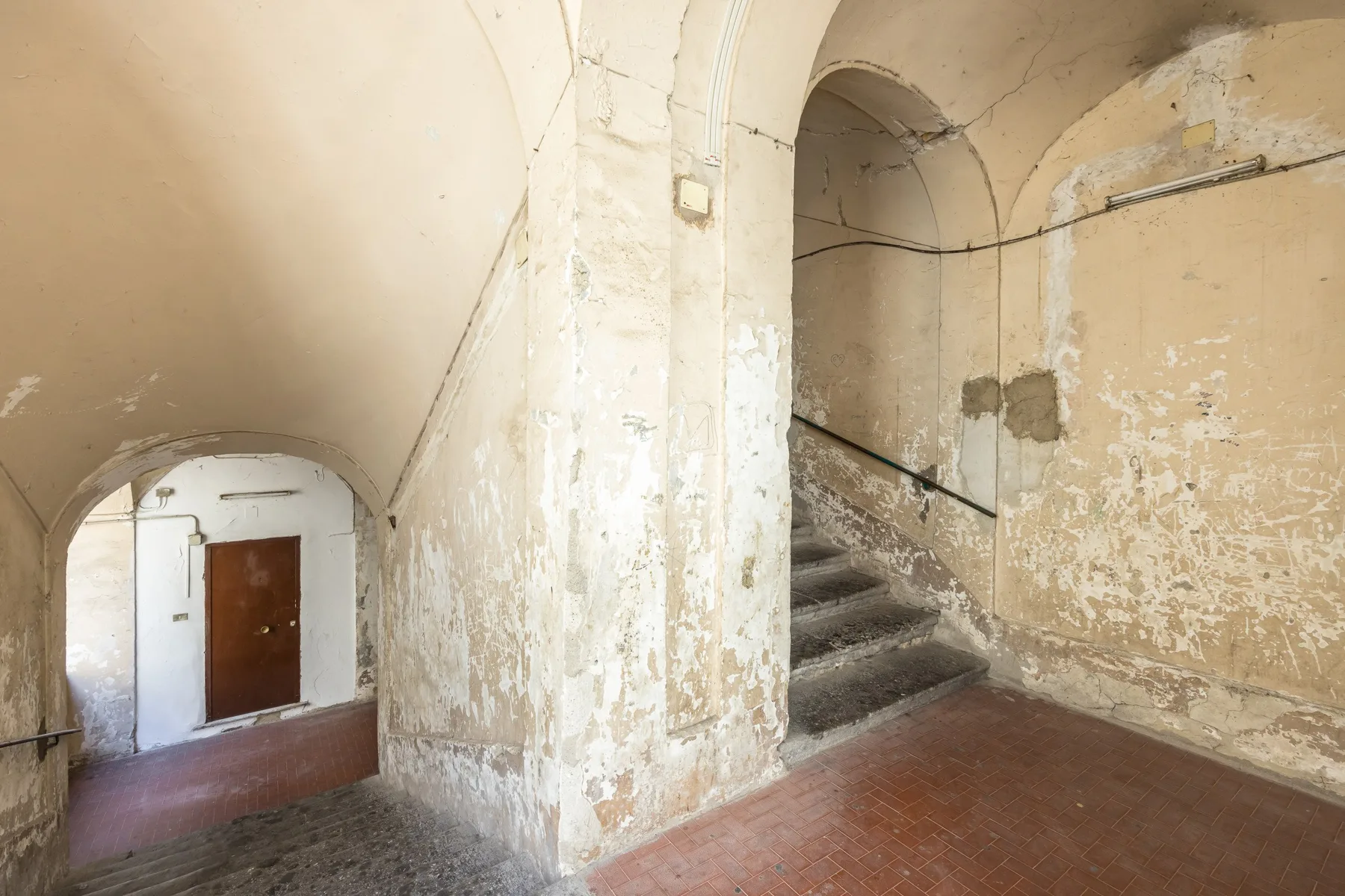 A worn interior hallway with an arched passage and stairs.