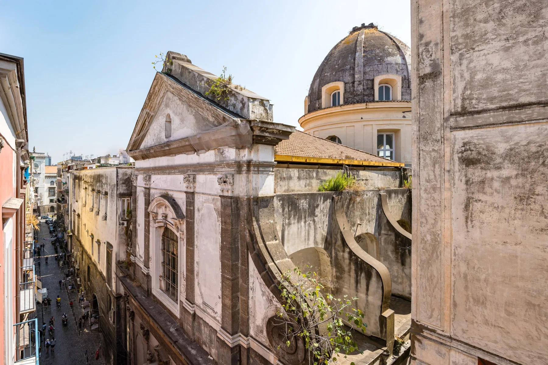 Historic stone buildings line a narrow urban street beneath a domed roof.