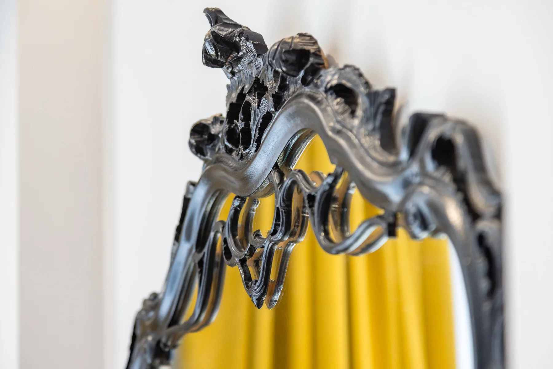 An ornate dark frame surrounds a mirror with a yellow reflection.