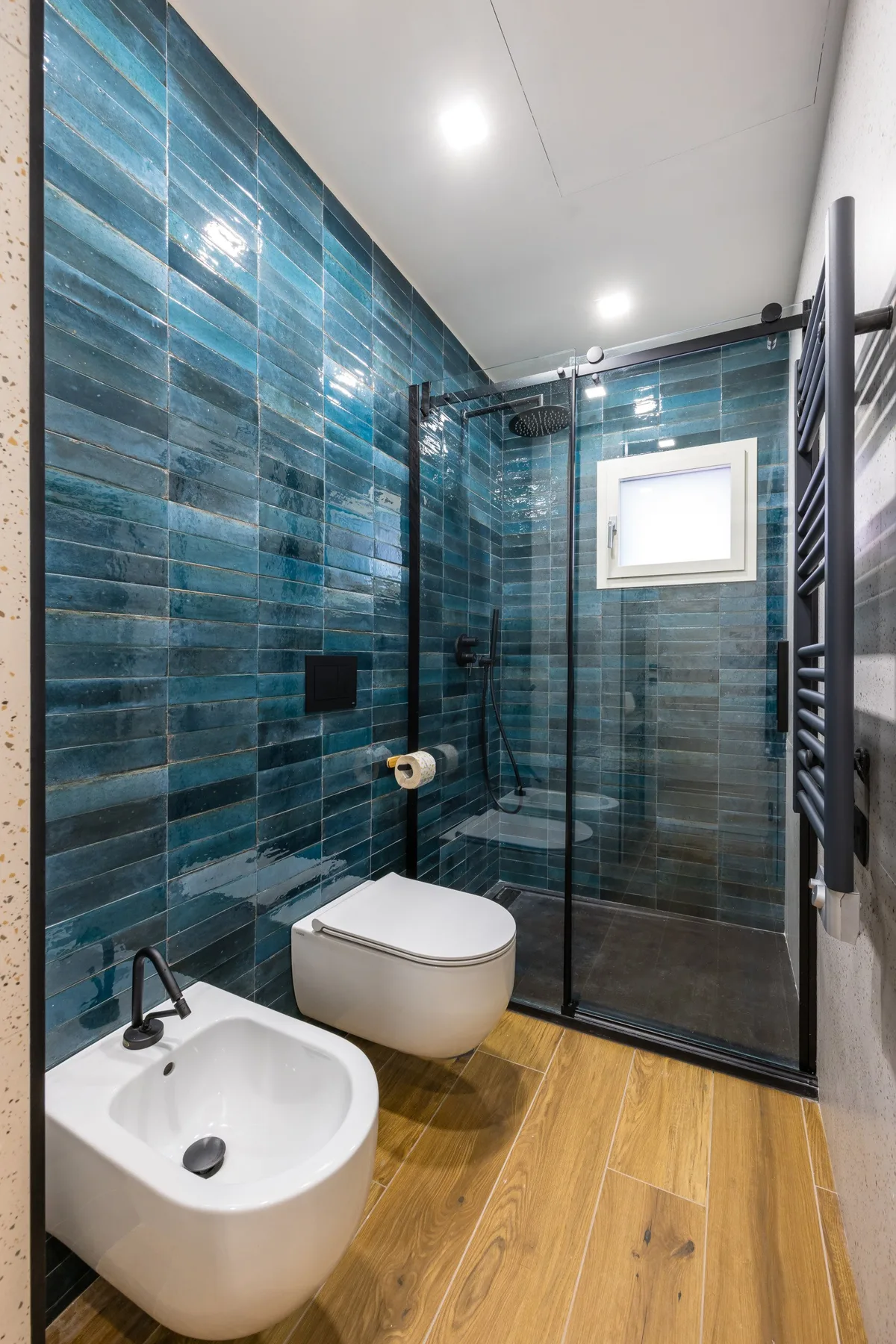 A bathroom with blue tiled walls, a shower, and a white basin.