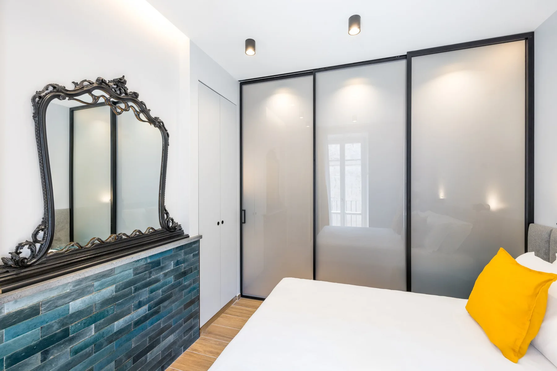 A bedroom with a bed and a large decorative mirror above a tiled wall.