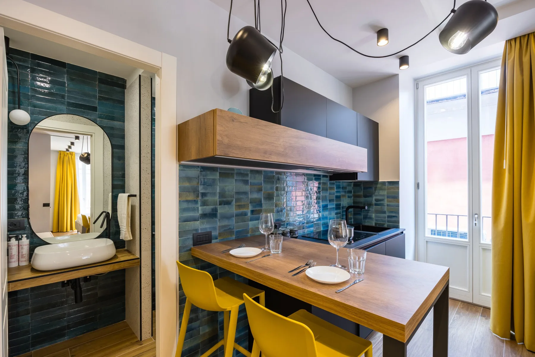 A dining area with a wooden table and yellow chairs sits beside a tiled bathroom.