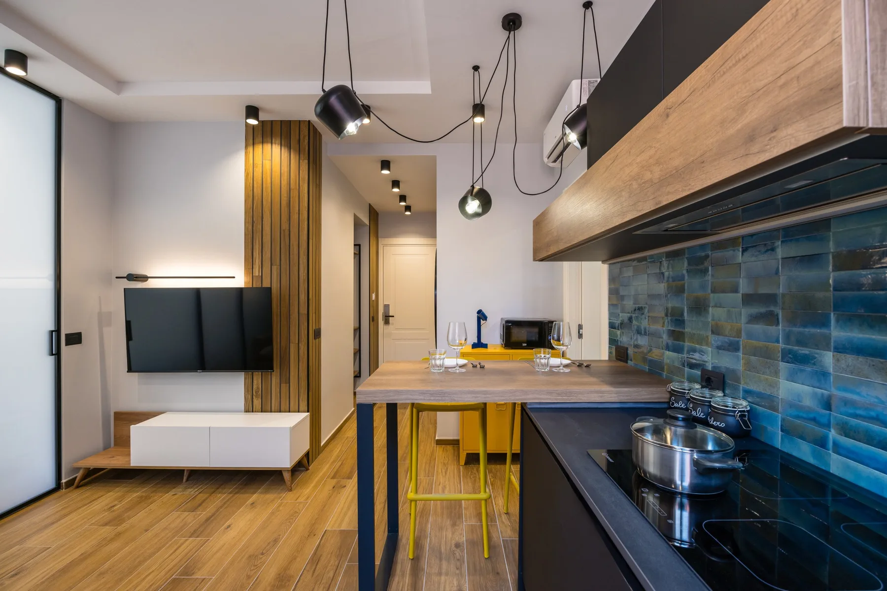A modern kitchen with a dining counter, pendant lights, and blue tile backsplash.