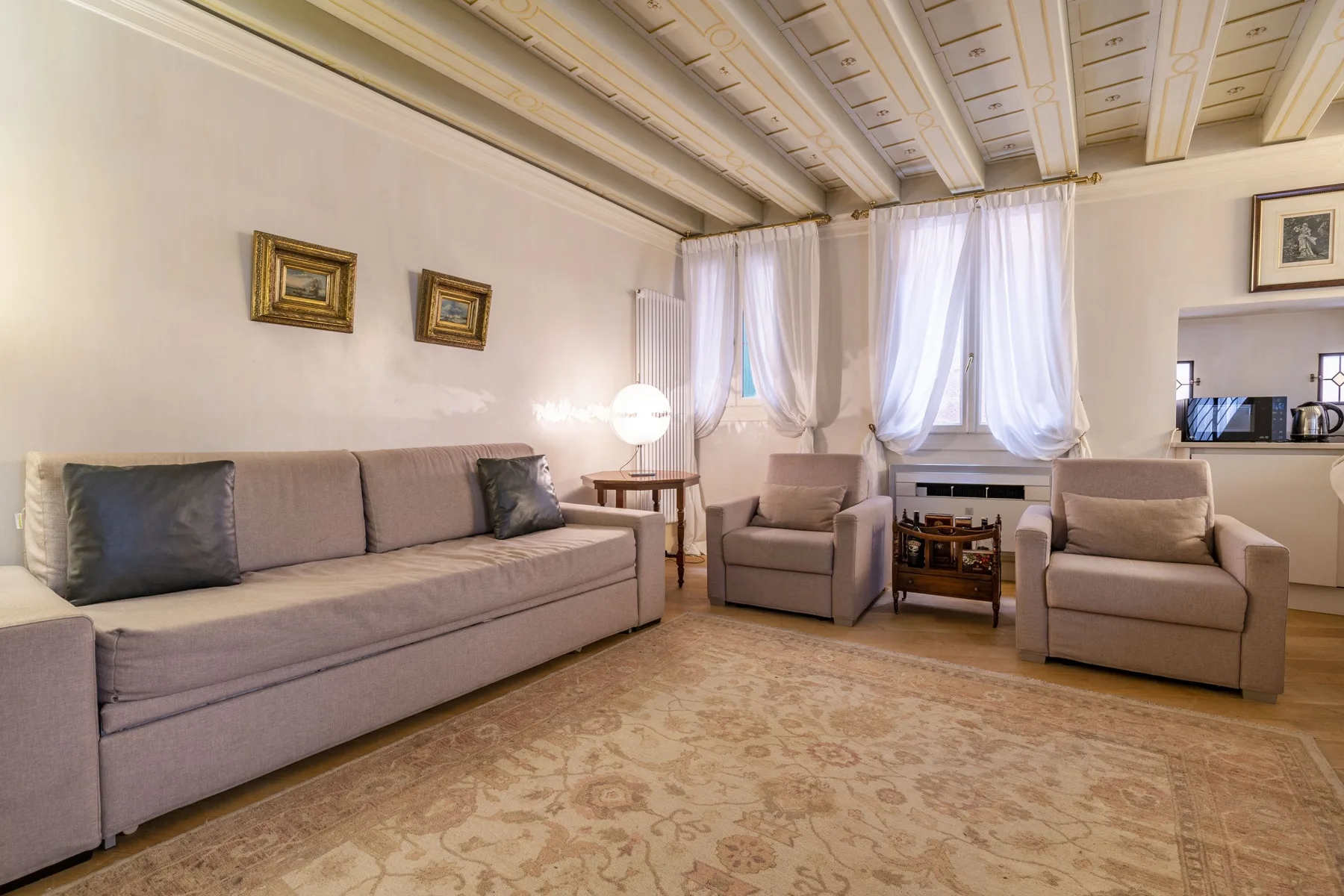 A living room with seating arranged around a small table beneath curtained windows.