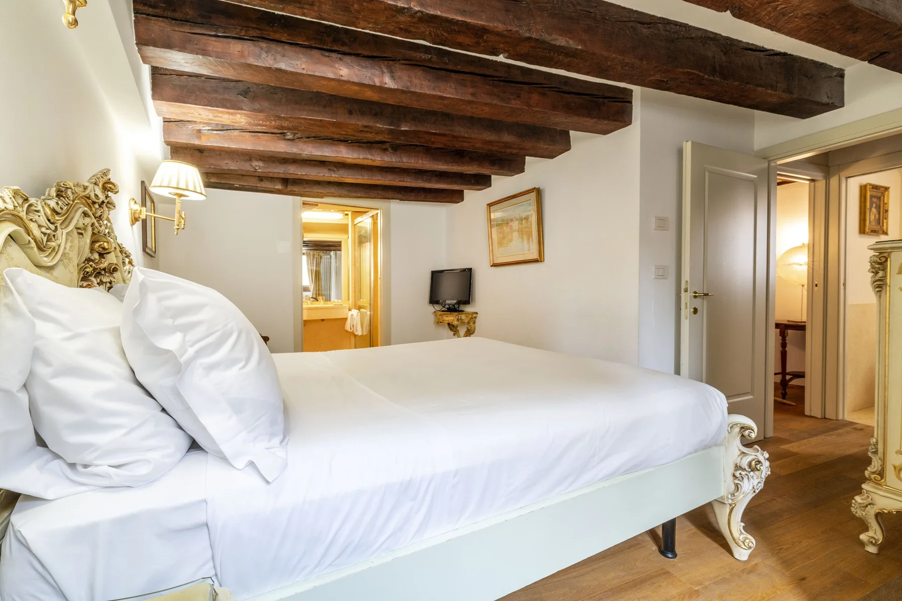 A bedroom with a large bed beneath exposed wooden ceiling beams.