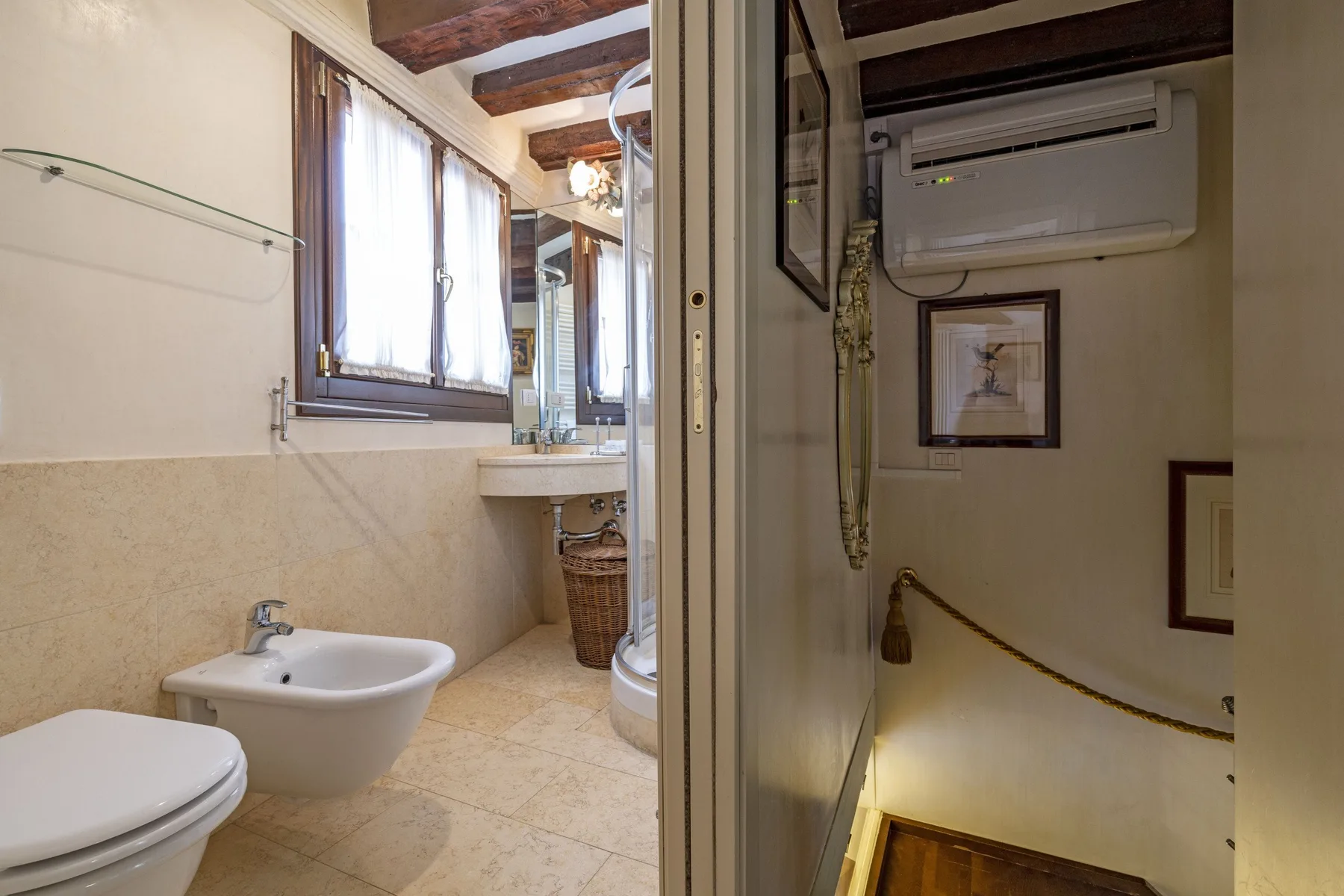 A bathroom with a sink, bidet, and window beside a stairwell.