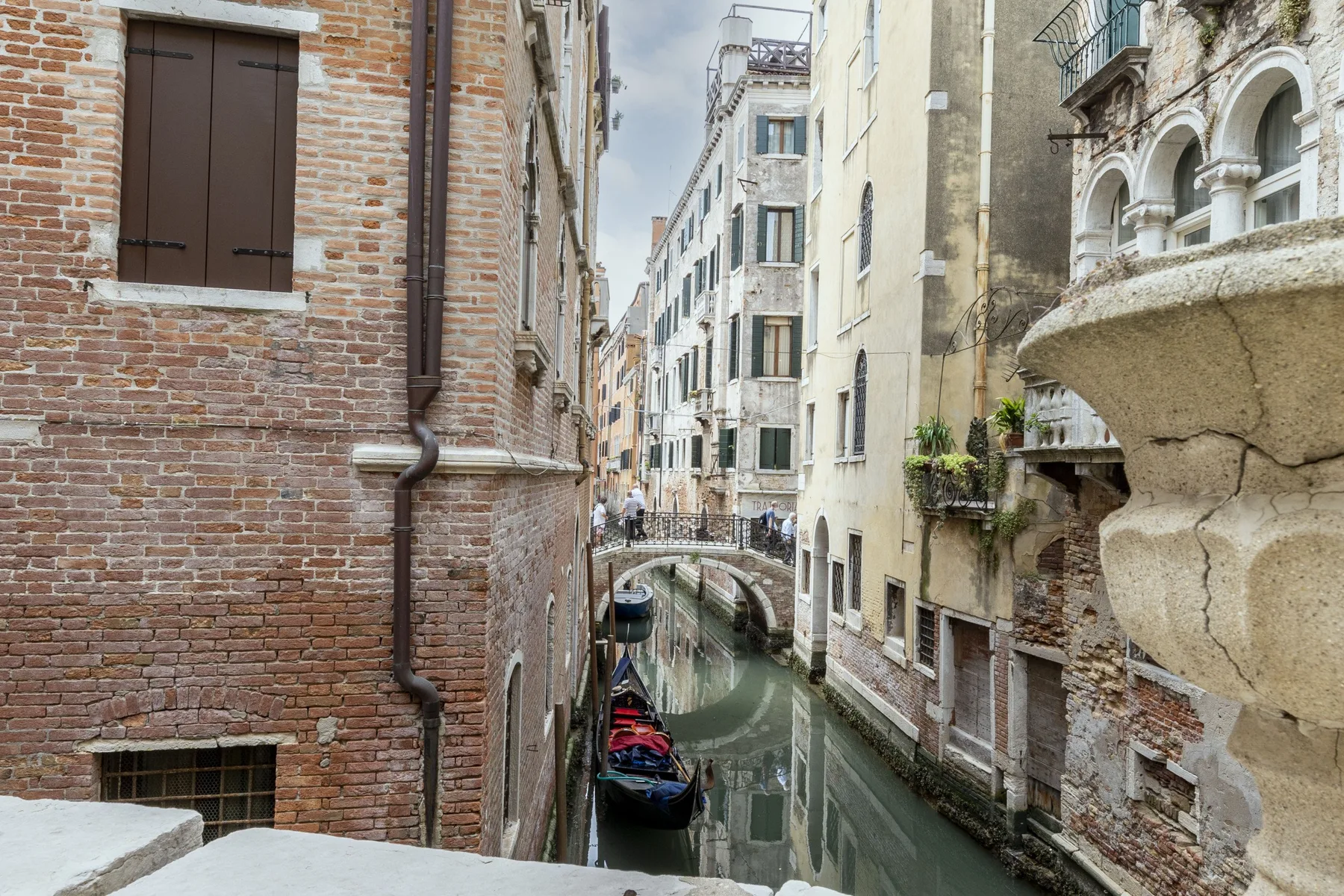 A narrow canal winds between closely spaced brick and stucco buildings.