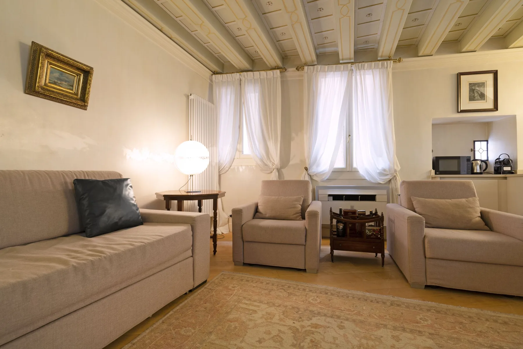 A living room with beige seating, sheer curtains, and a small table.