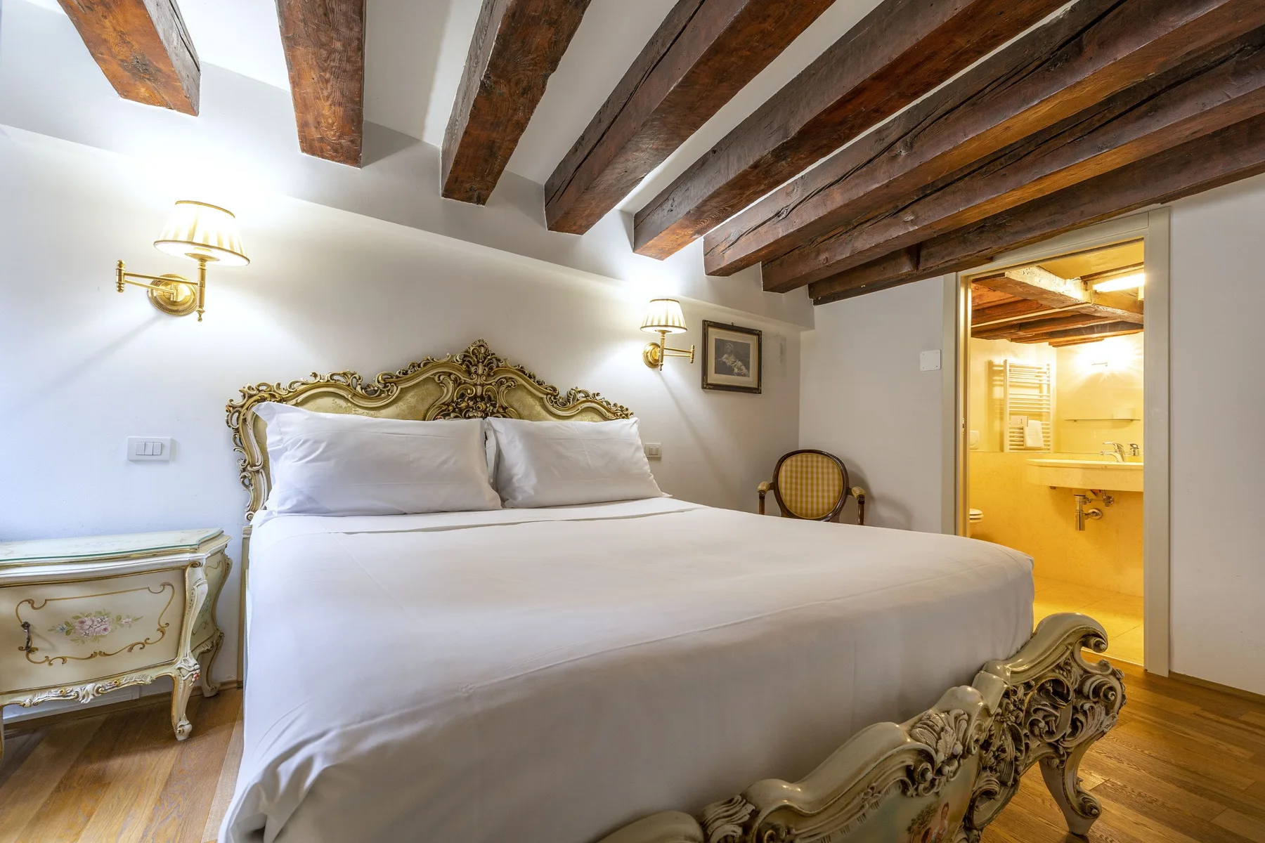 A bedroom with an ornate bed beneath exposed wooden ceiling beams.