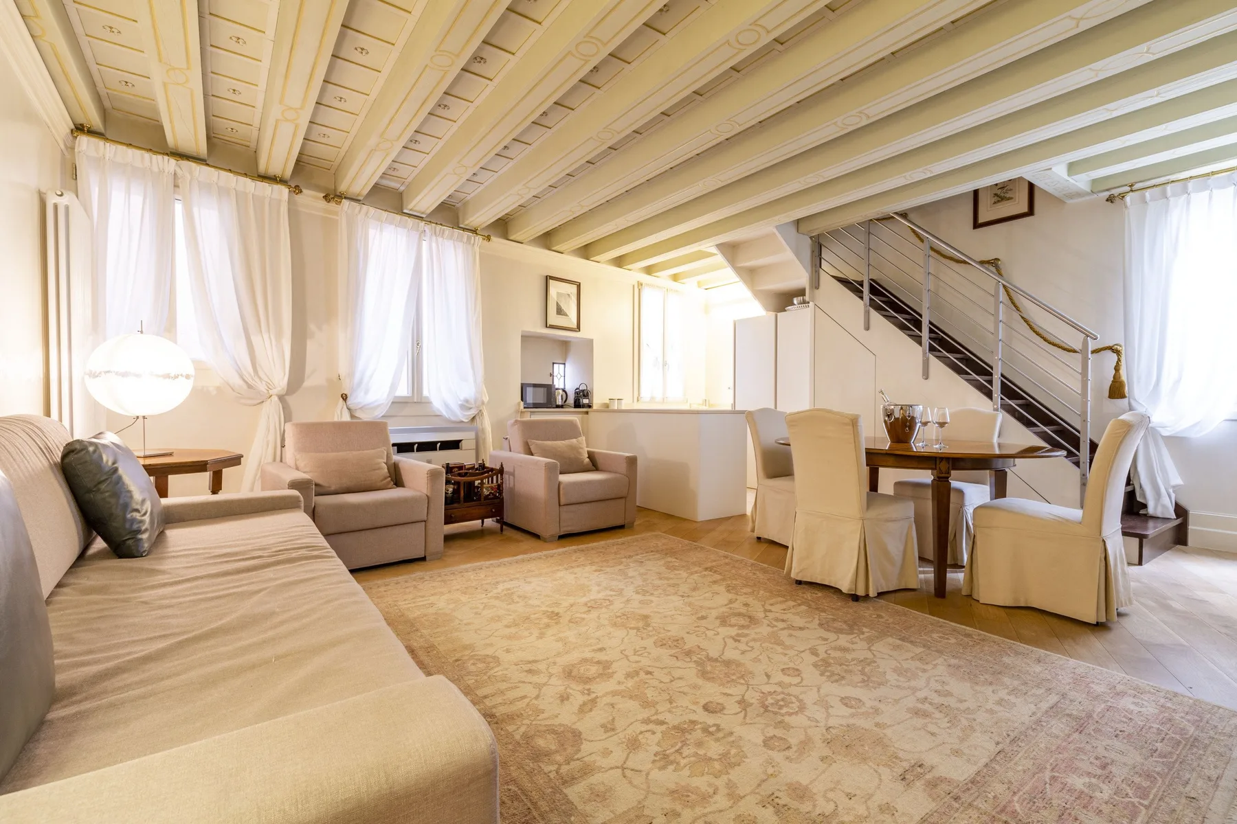 A bright living and dining area with seating, a table, and a staircase.