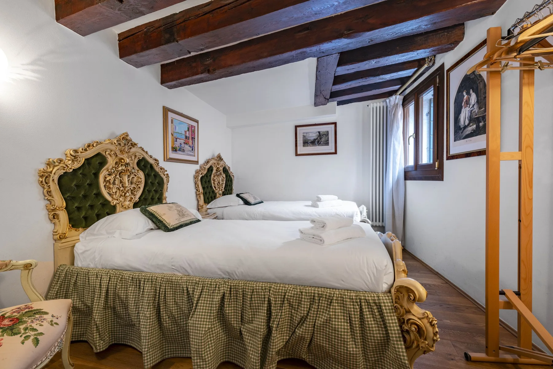 A bedroom with two beds, ornate green headboards, and exposed wooden ceiling beams.