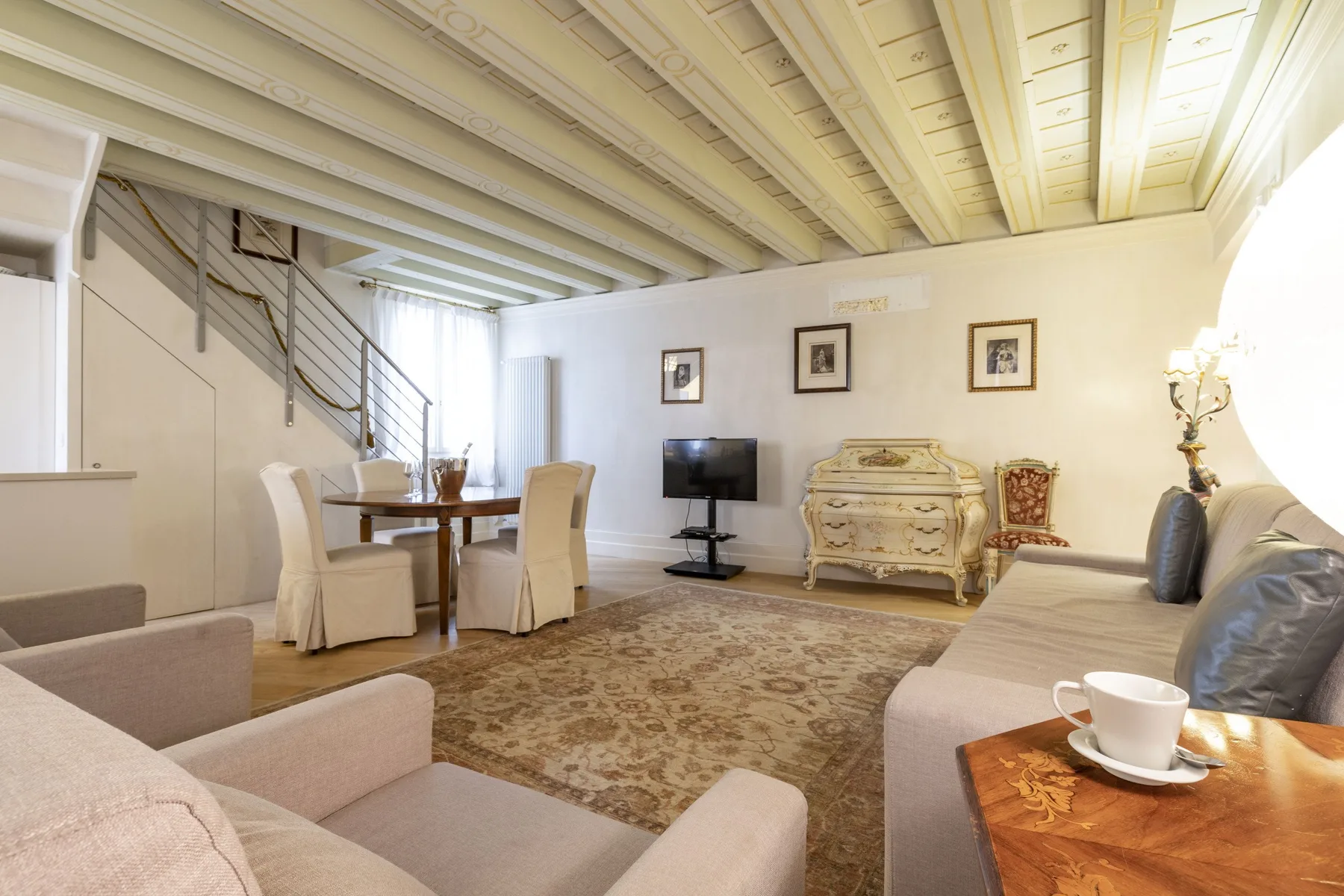 A bright living and dining area with a patterned rug and a television.