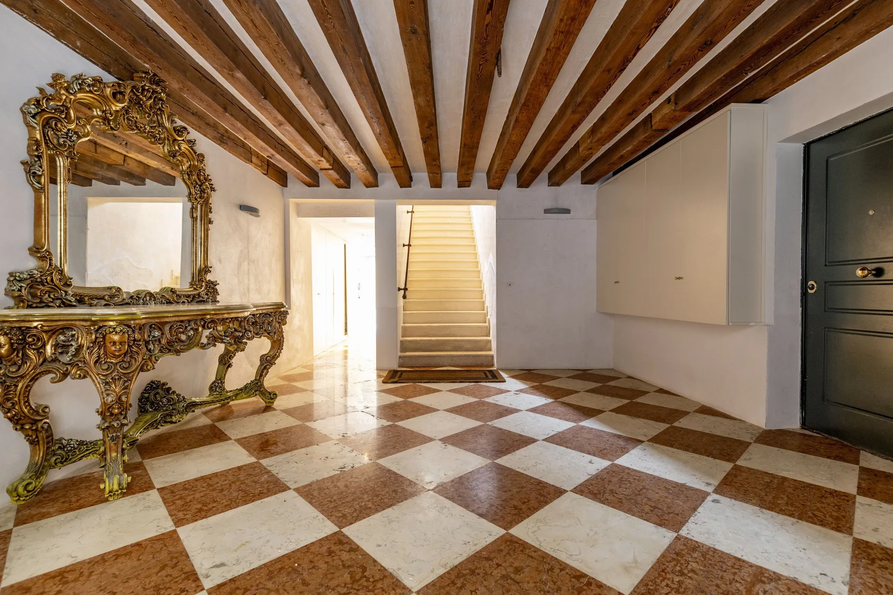 A tiled entry hall with an ornate console table, mirror, and staircase.