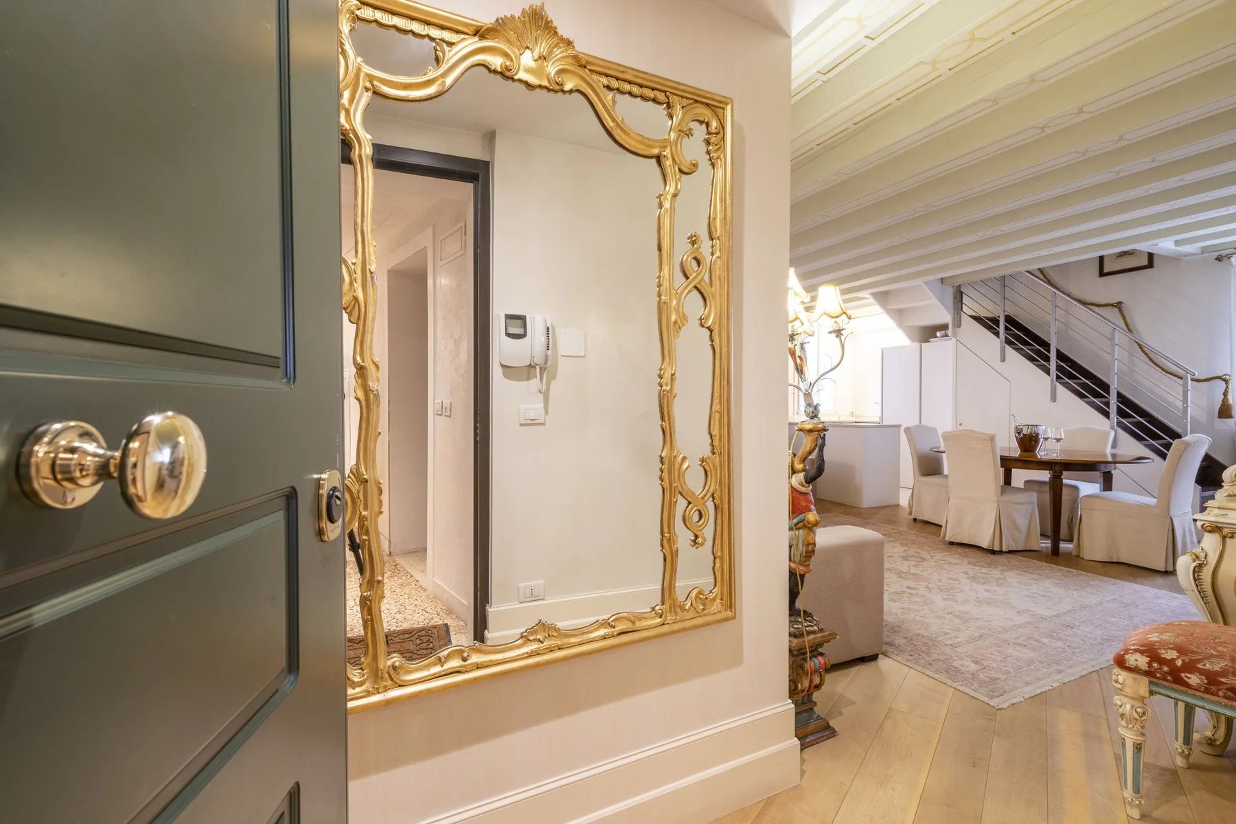An elegant dining area with a table and staircase beside a large gold-framed mirror.