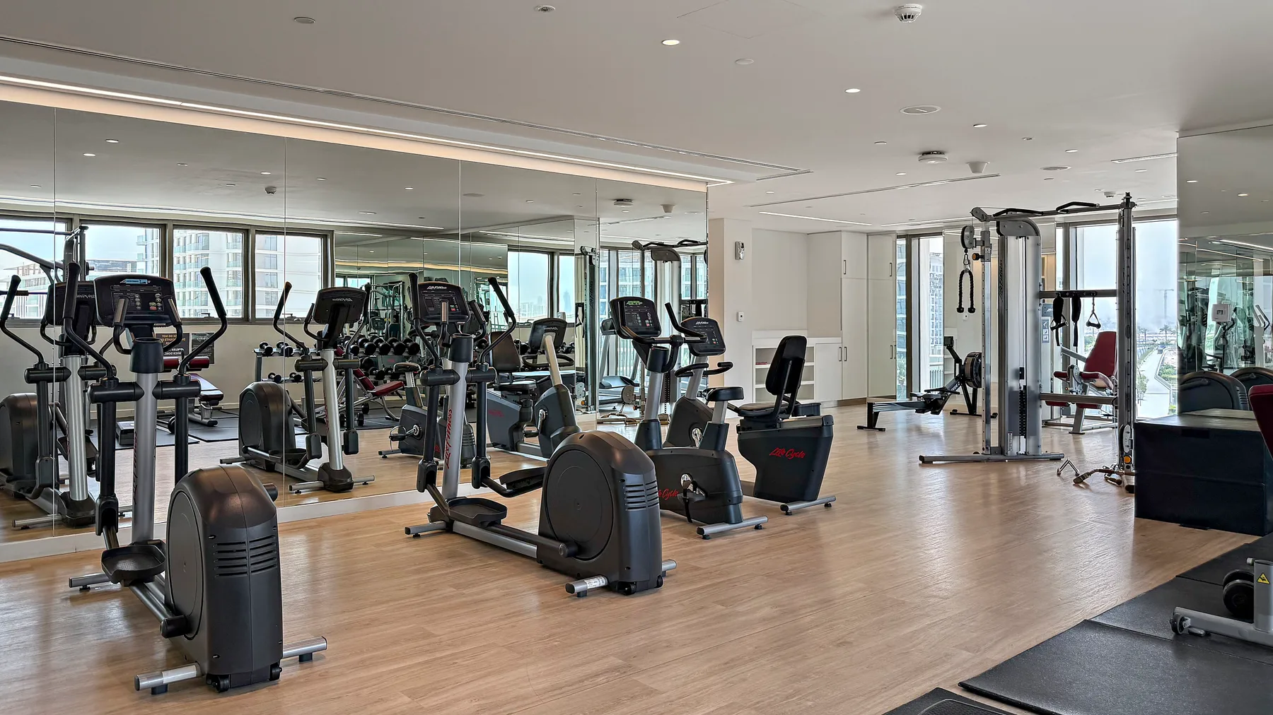 Un gimnasio luminoso con máquinas de ejercicio sobre un suelo de madera.