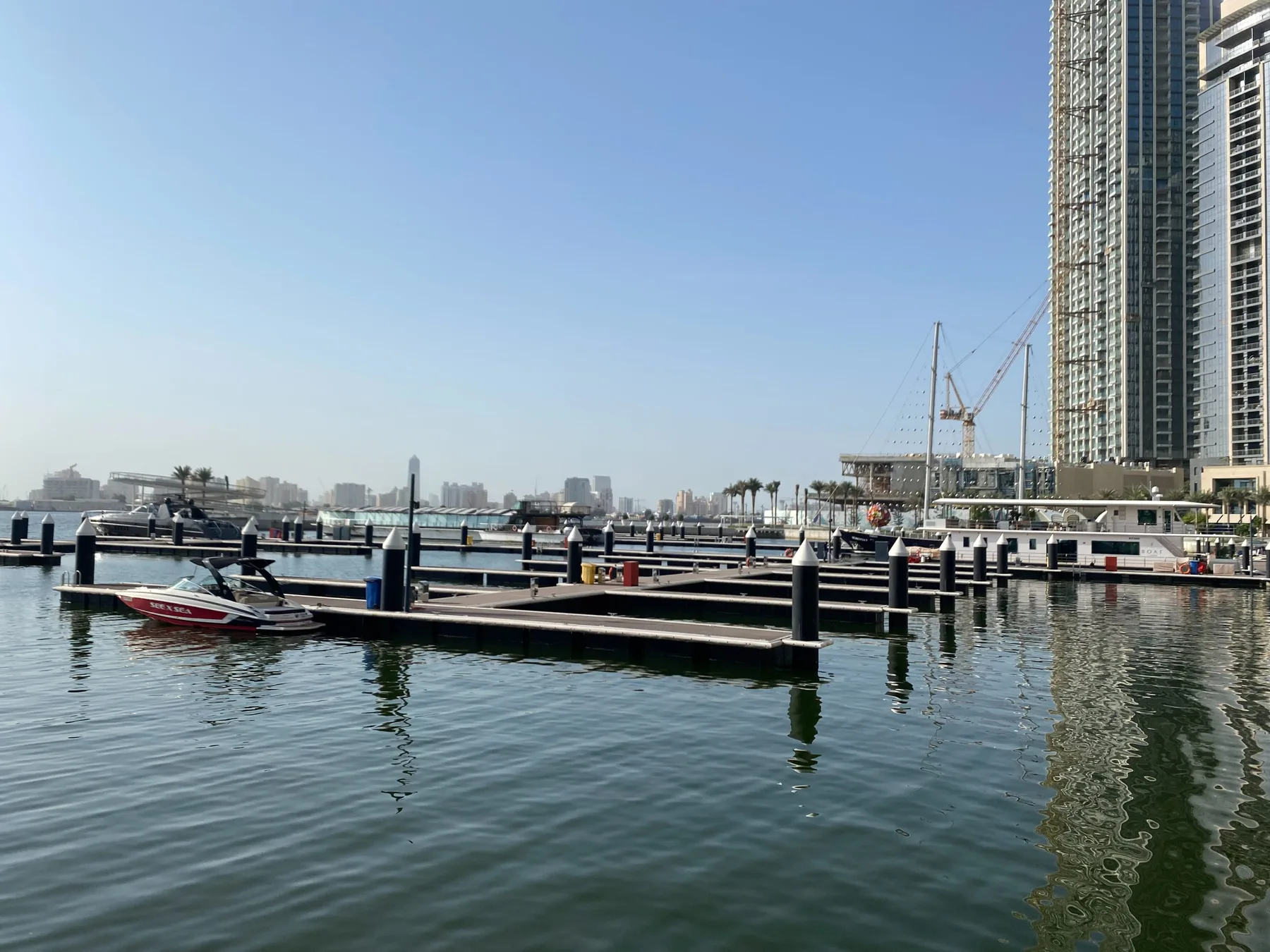Una marina con muelles flotantes y embarcaciones junto a altos edificios frente al agua.