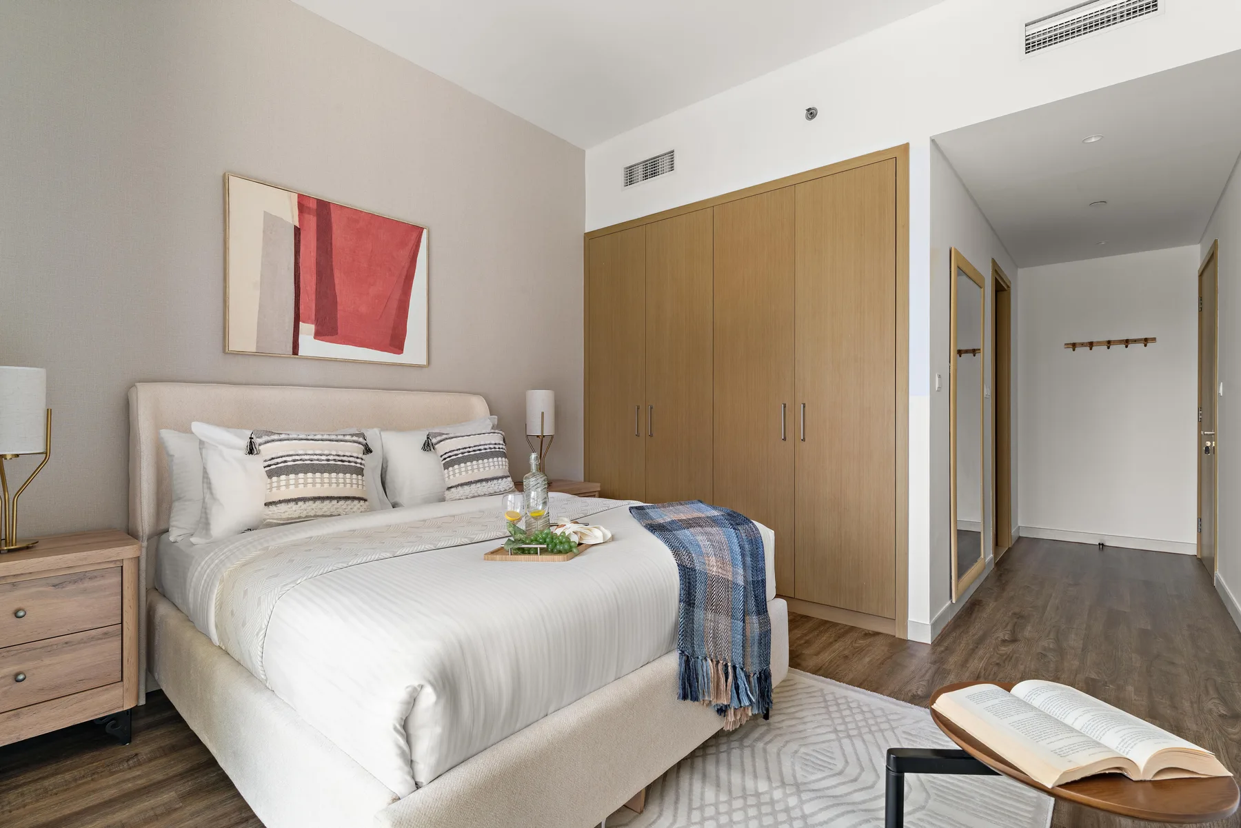 Un dormitorio con una cama arreglada, una obra enmarcada y un armario de madera.