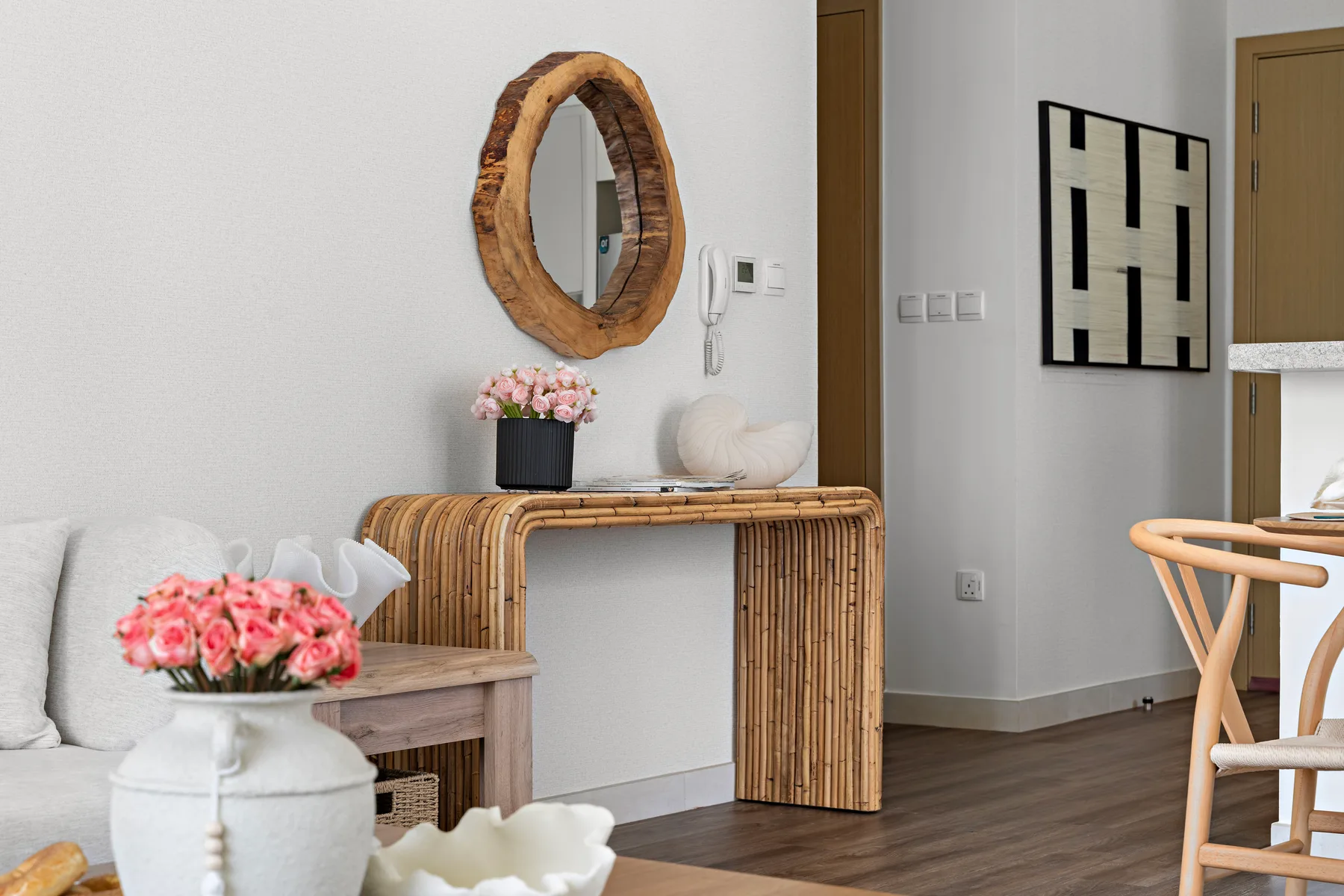 Una sala luminosa con una consola de madera, un espejo ovalado y asientos.