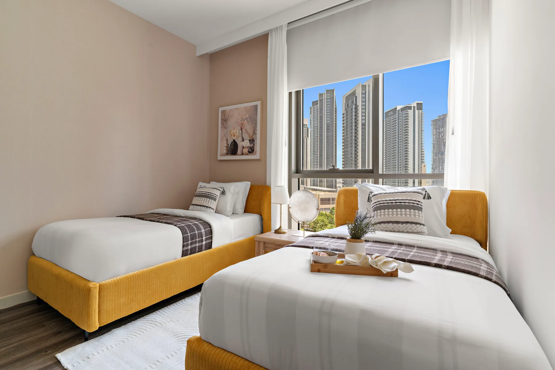 Un dormitorio con dos camas junto a una ventana amplia con vistas a edificios altos.