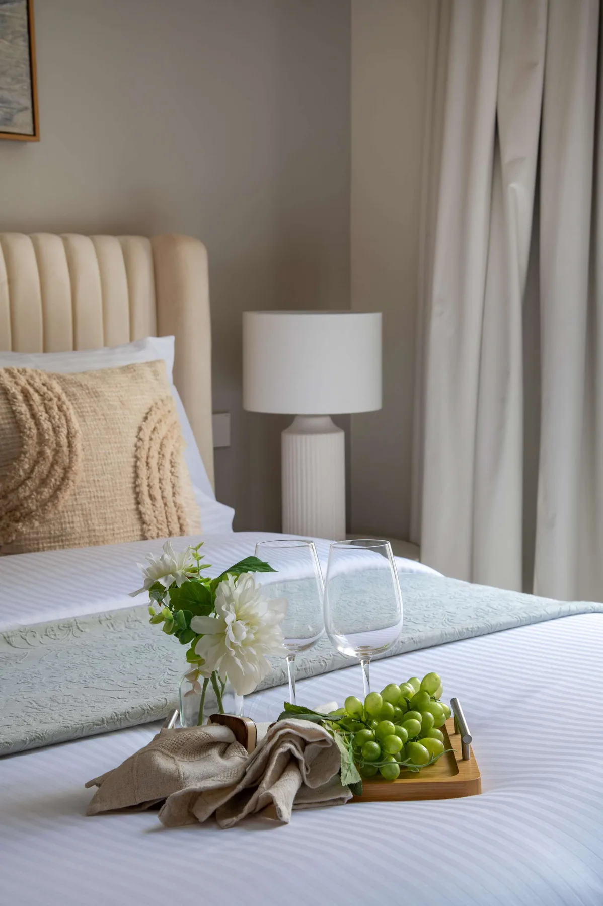 Un dormitorio con una cama bien tendida, flores frescas y uvas en una bandeja.