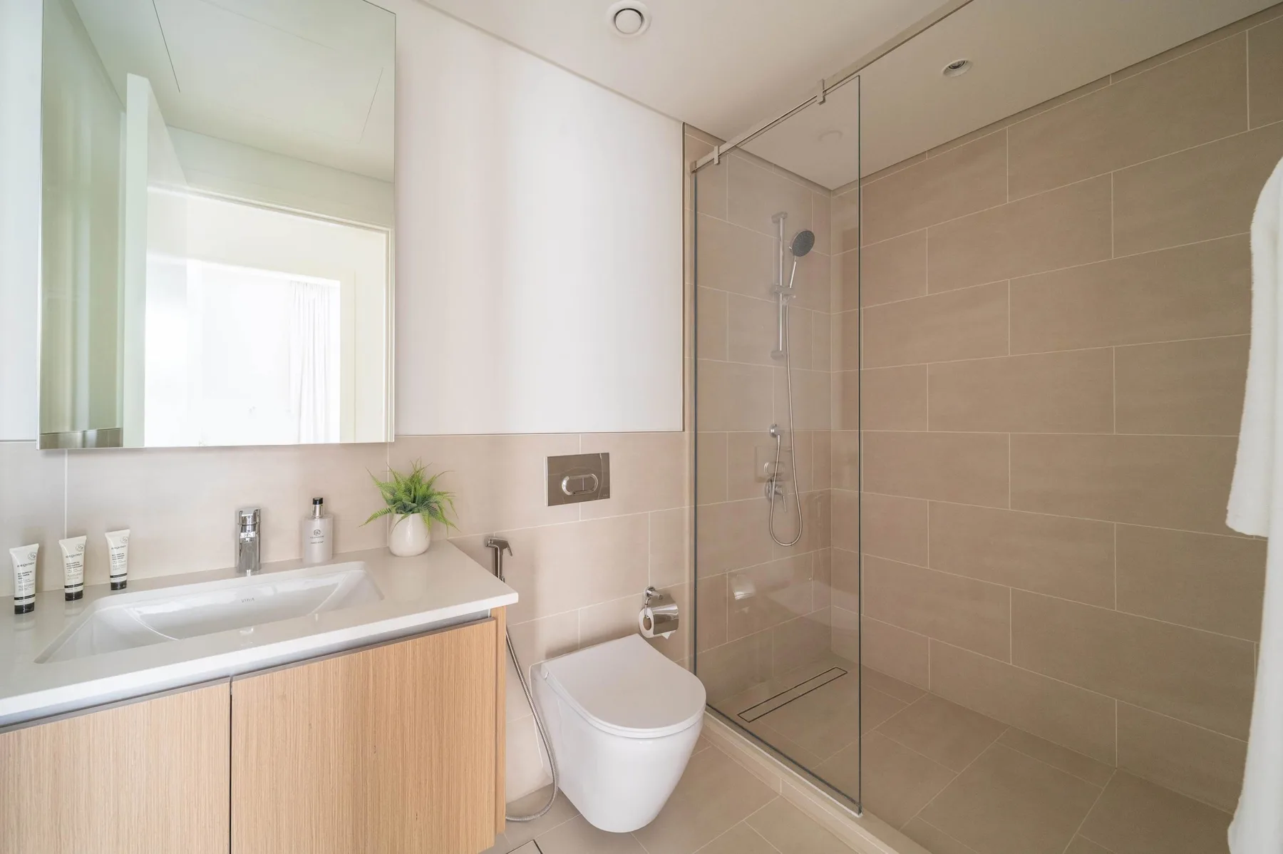 Un baño luminoso con lavabo, inodoro y ducha con mampara de vidrio.
