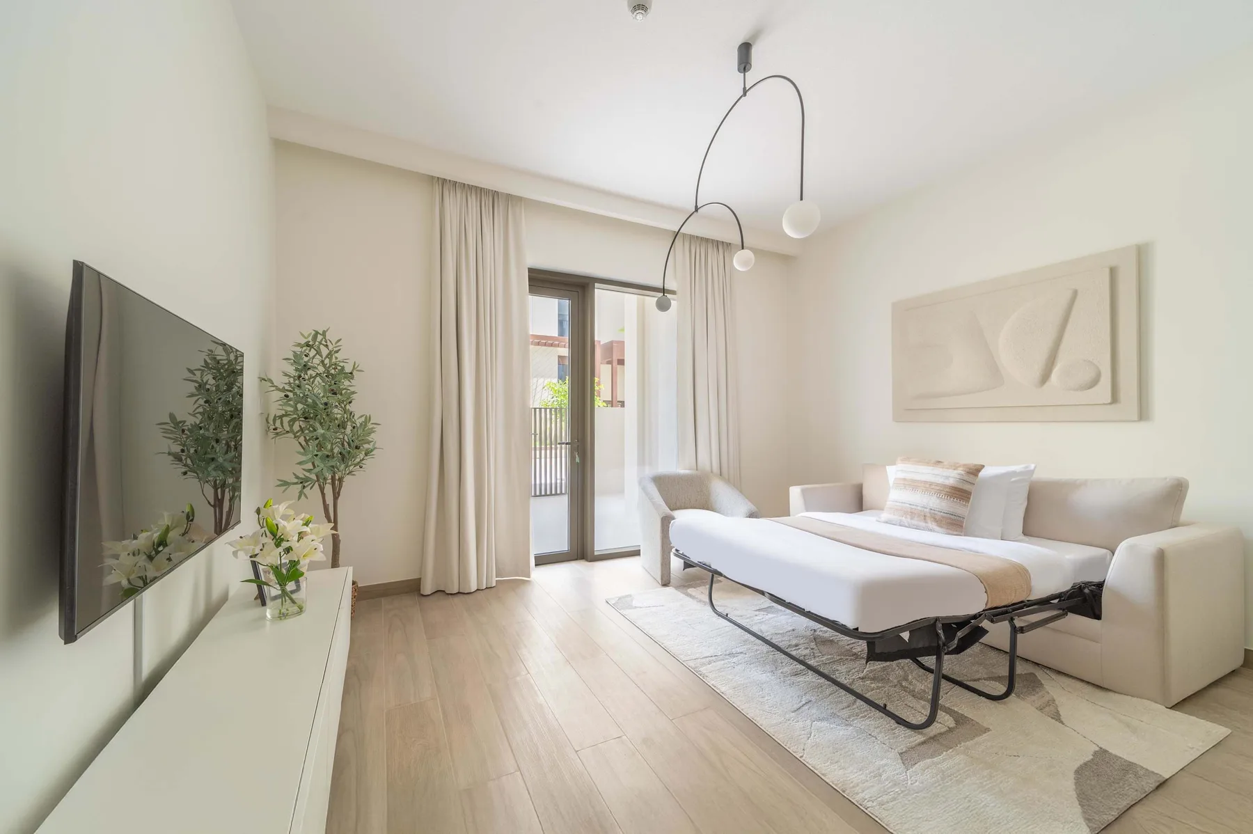 Una sala luminosa con televisor, asientos y puertas de vidrio que dan a un balcón.