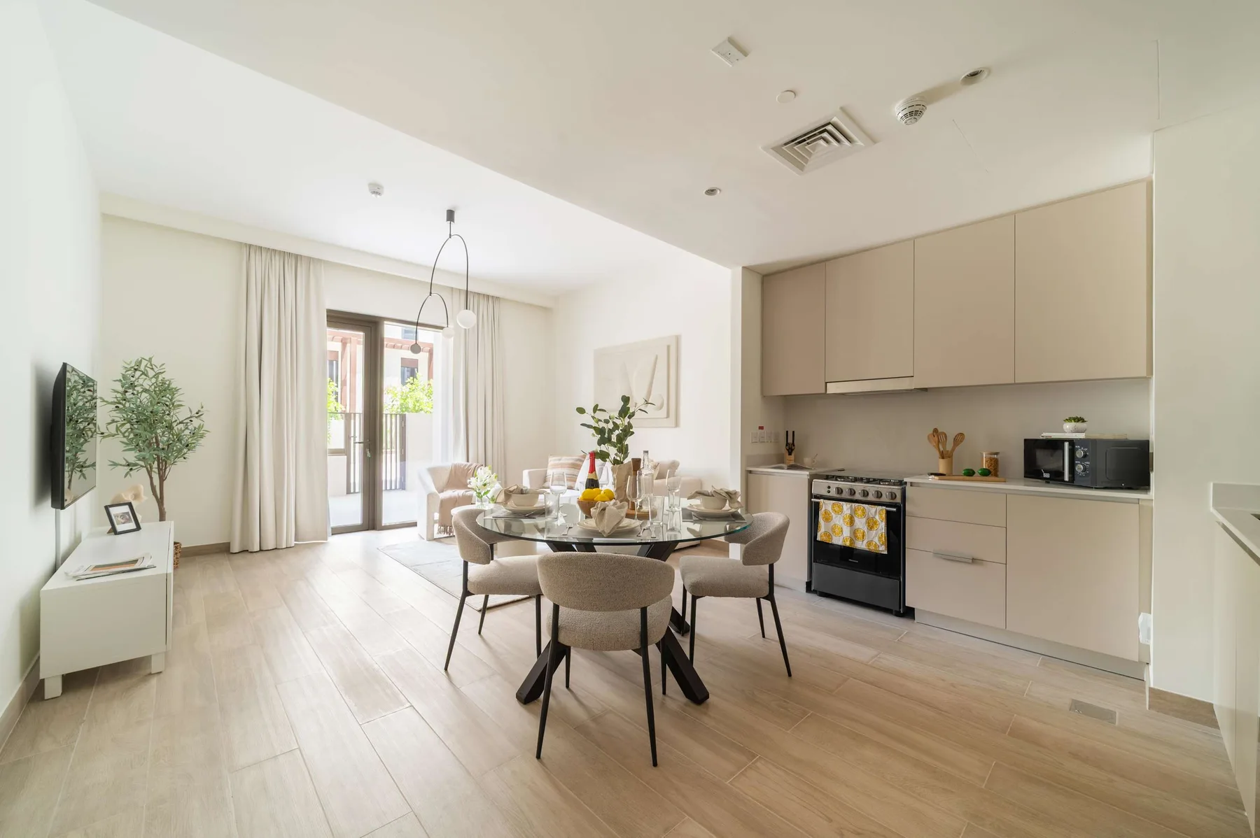 A bright open-plan dining area and kitchen with a round table and light cabinetry.