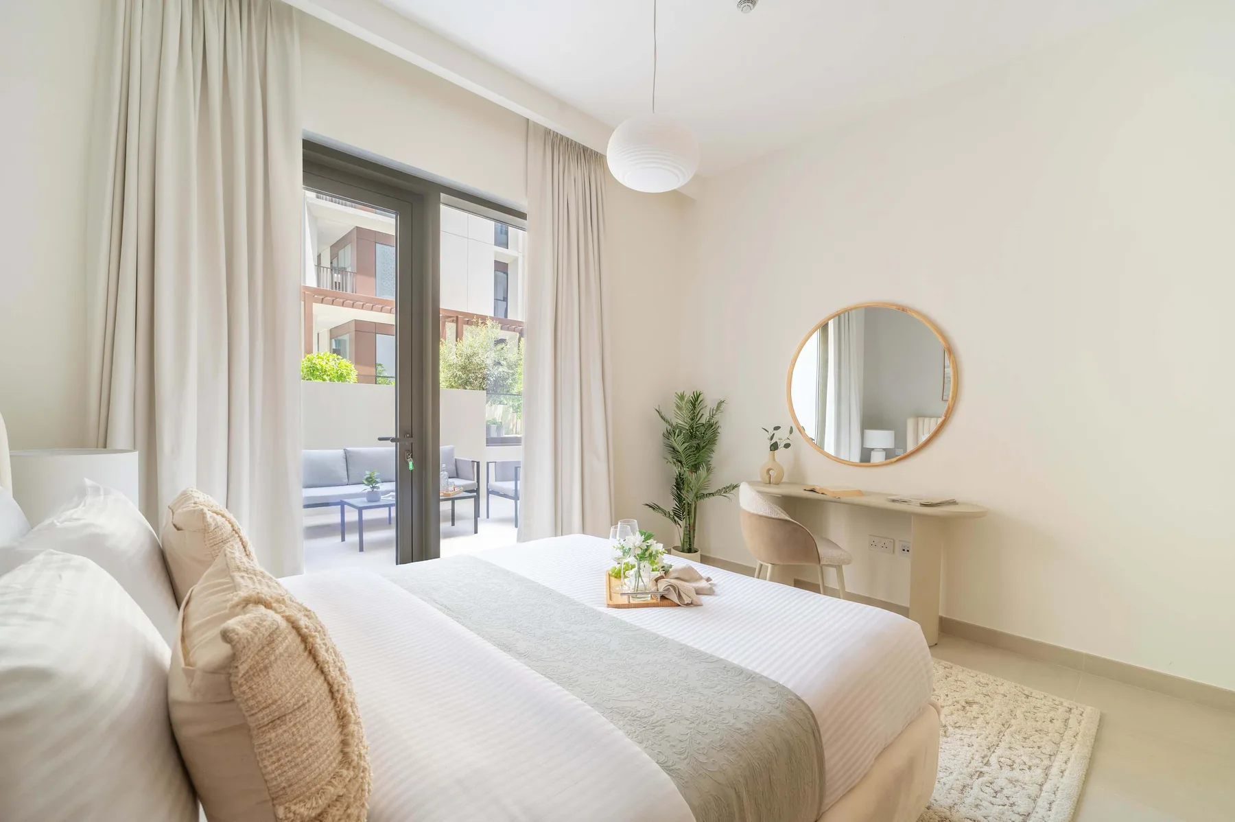 Un dormitorio luminoso con una cama, un tocador y un espejo redondo en la pared.