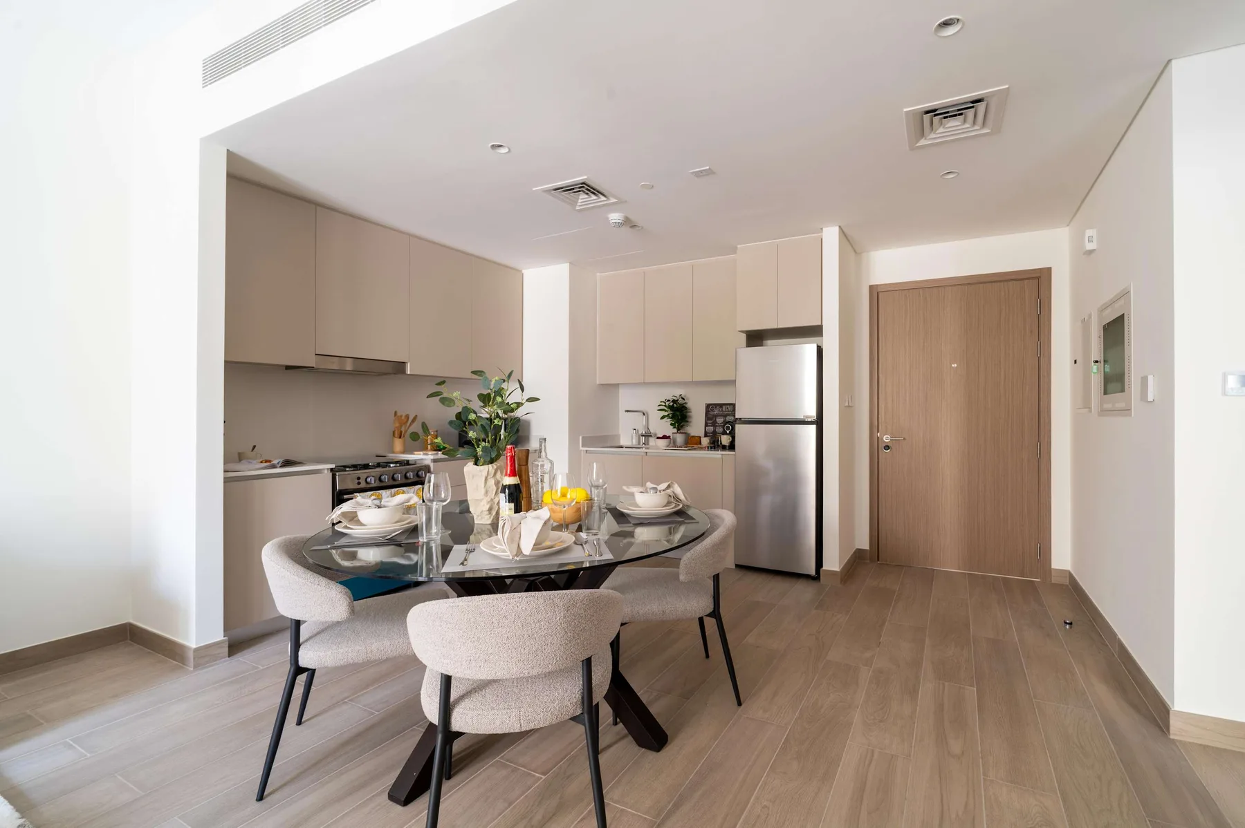 Un comedor con una mesa de vidrio está junto a una cocina compacta.