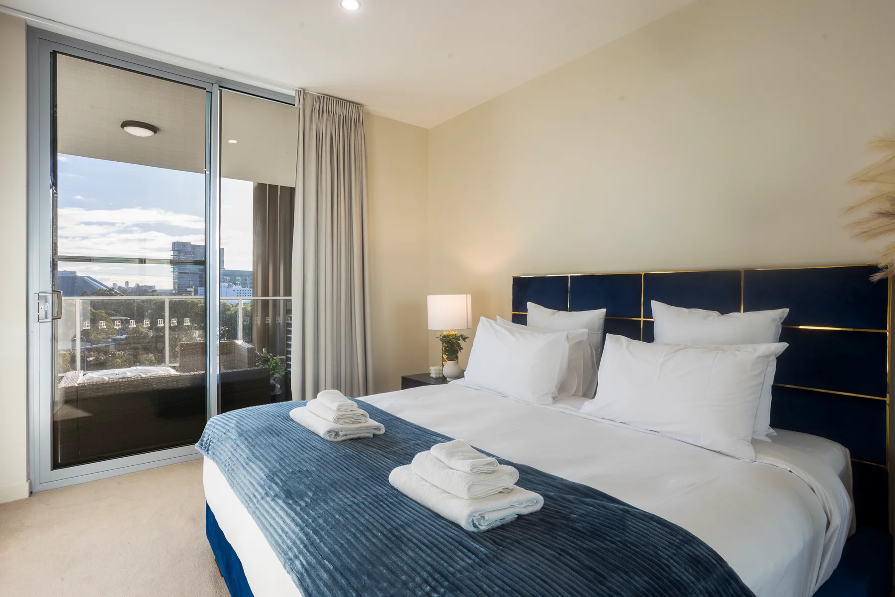 Un dormitorio luminoso con una cama bien tendida junto a una gran puerta de vidrio.