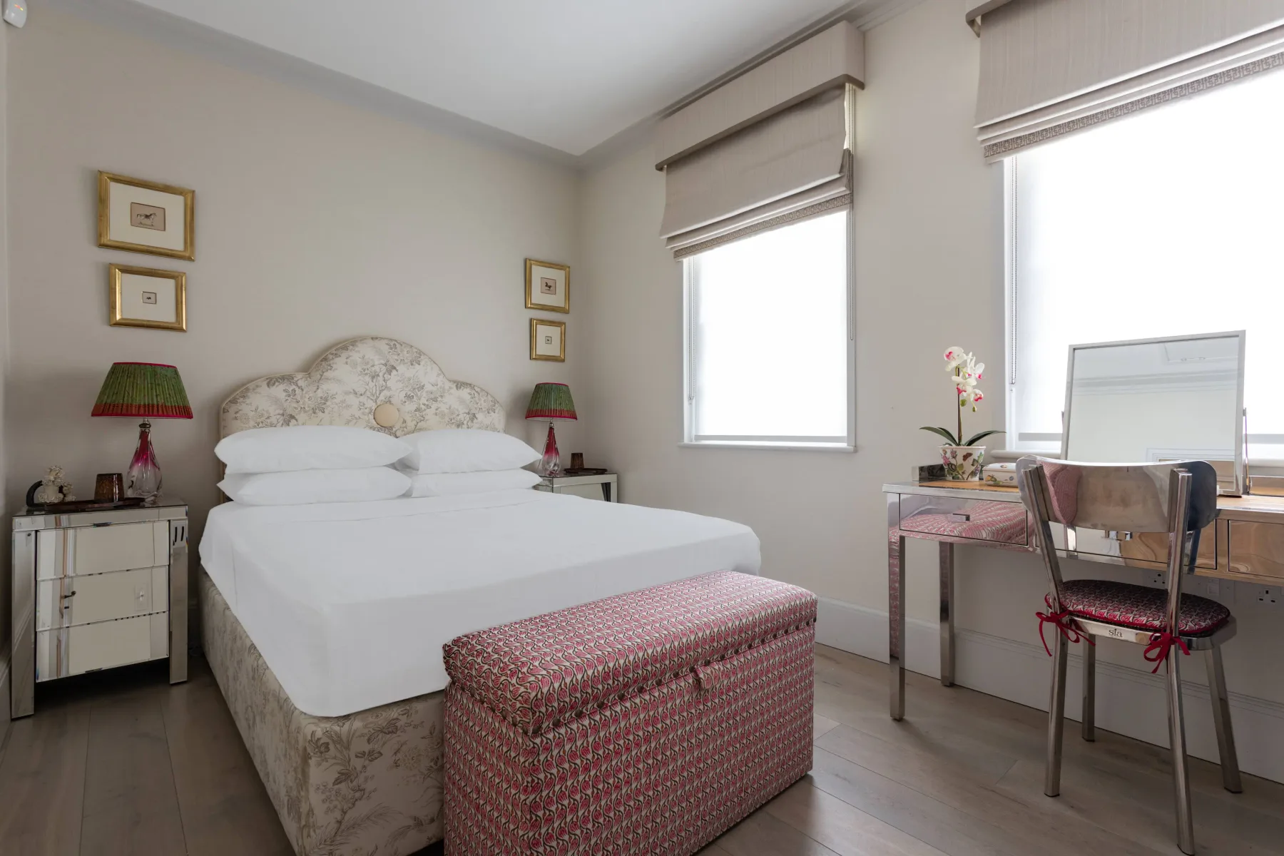 Un dormitorio con una cama bien tendida y un escritorio junto a las ventanas.