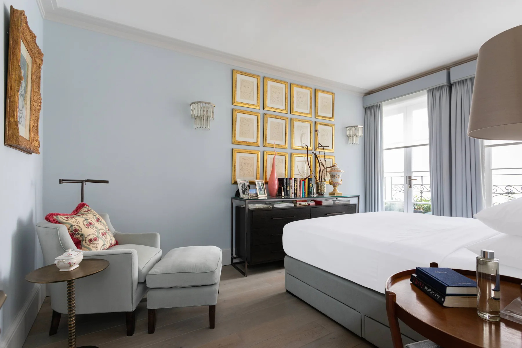 Un dormitorio luminoso con una cama tendida, una zona de estar y ventanas altas.