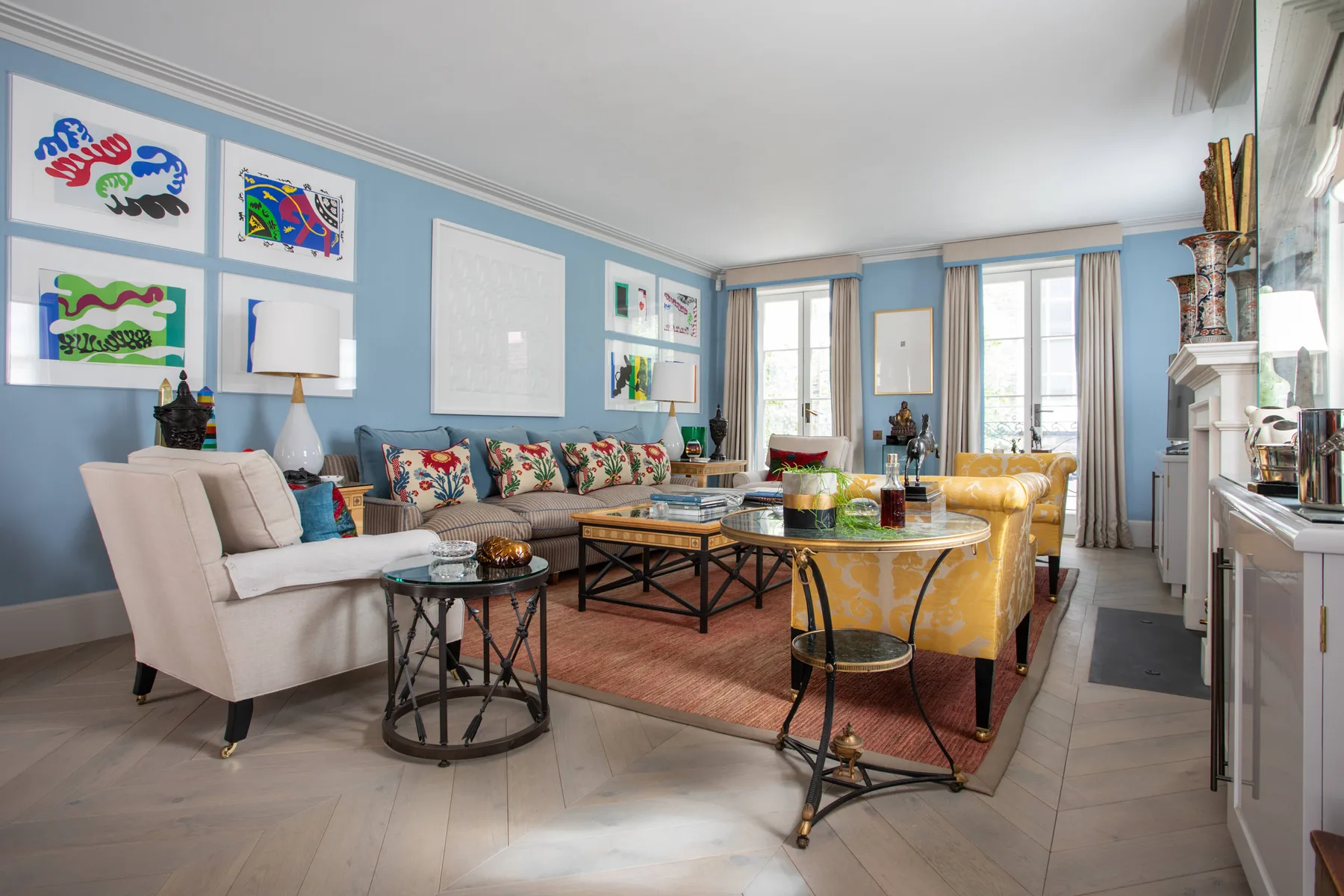 A bright living room with colorful seating, framed artwork, and large windows.