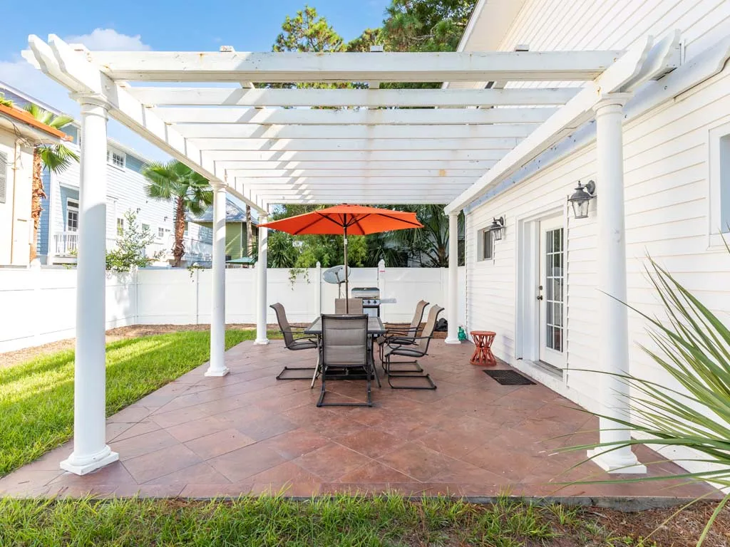 An outdoor patio with a dining table beneath a white pergola.