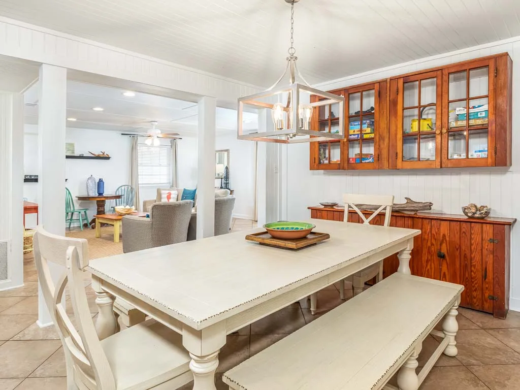 A bright dining area with a long table and wooden glass-front cabinets.