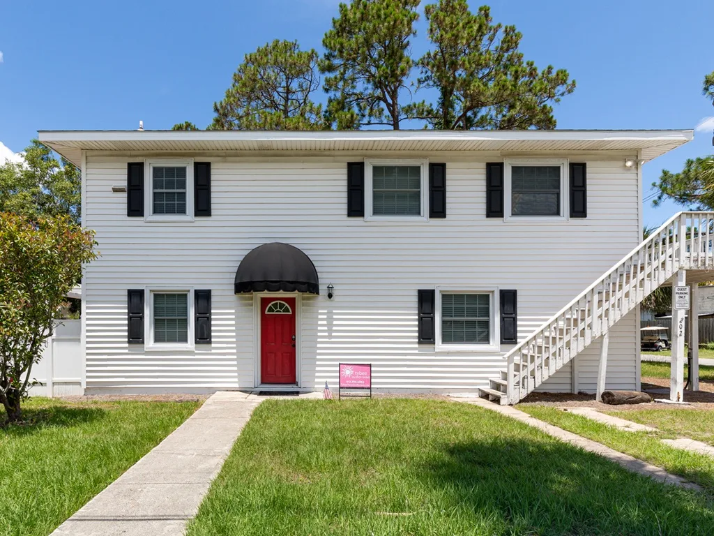 A white two-story building with a red entrance door and exterior staircase.