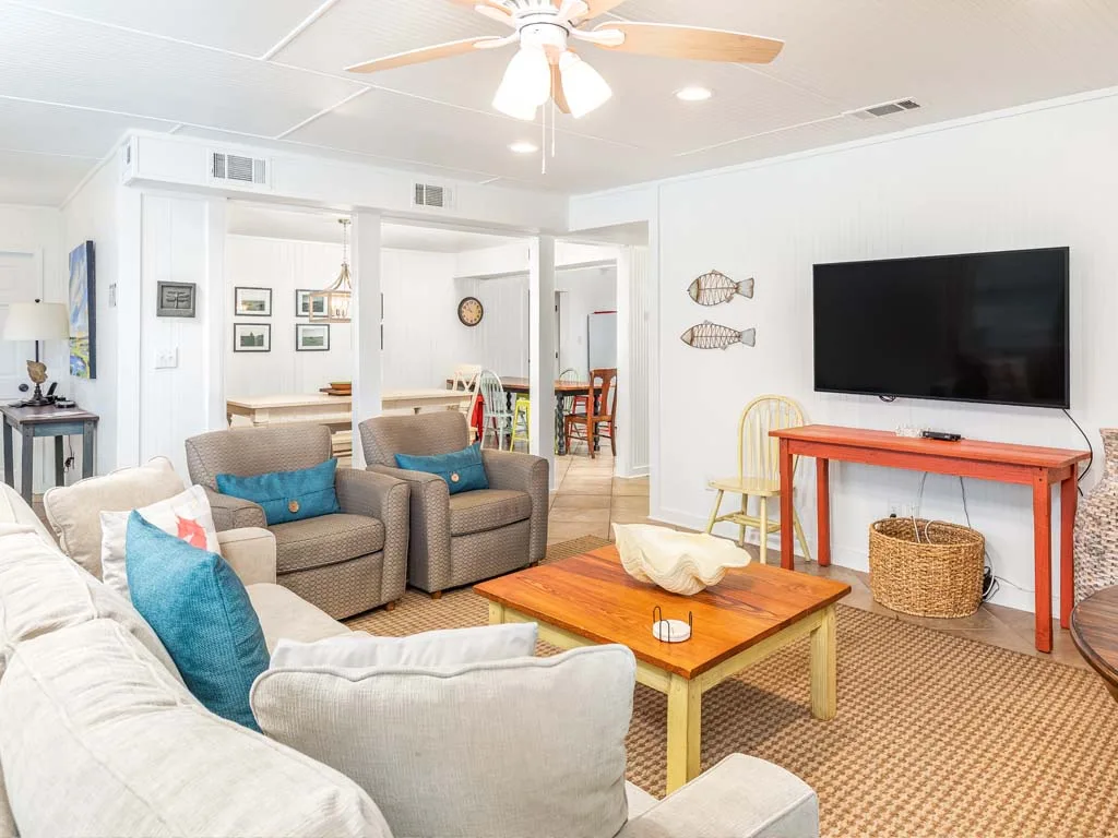 A bright living room with seating, a wooden coffee table, and a wall-mounted television.