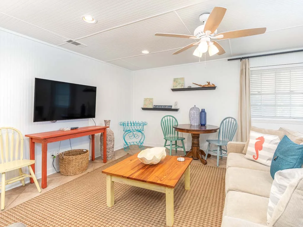 A bright living room with seating, a coffee table, and a wall-mounted television.