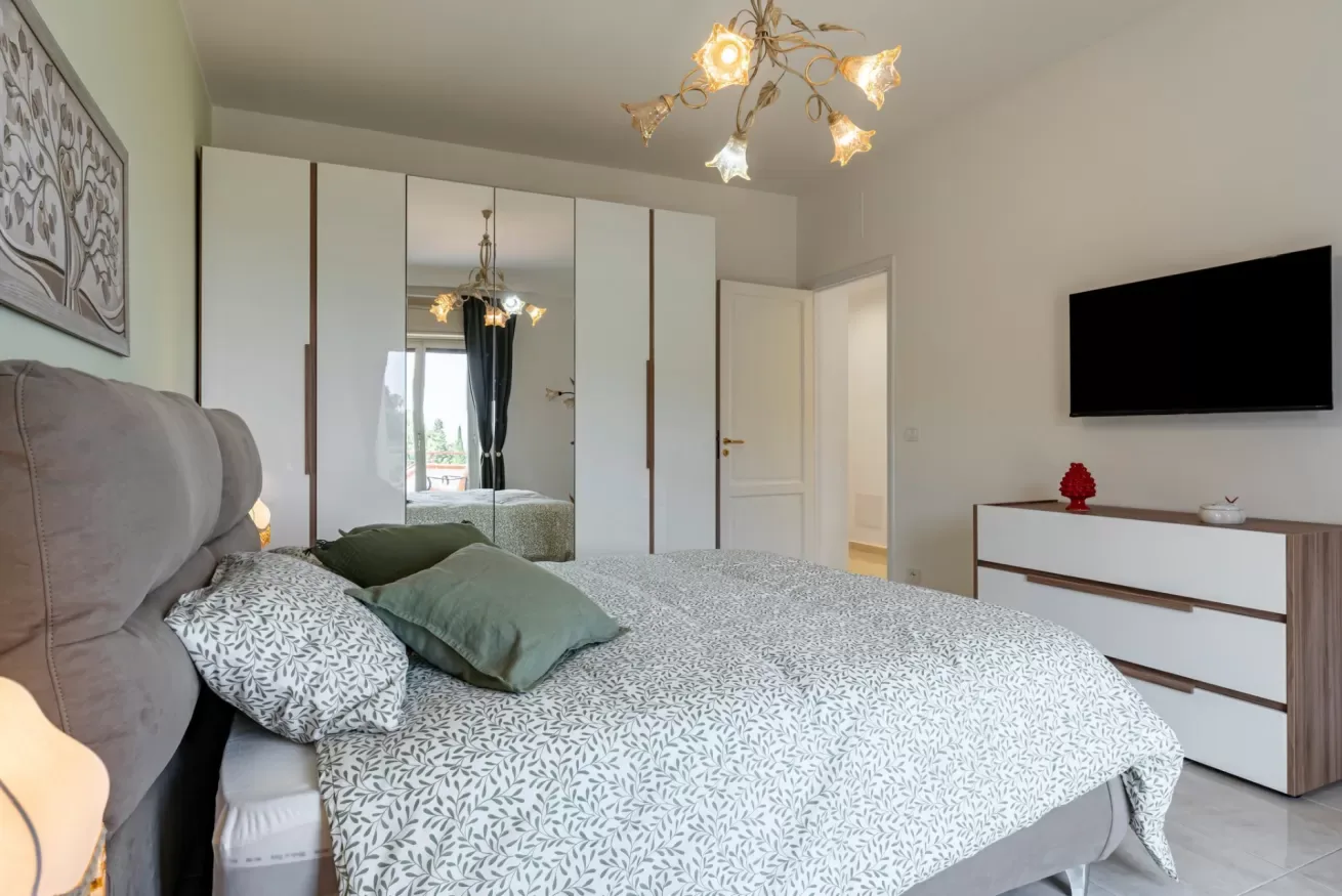 Un dormitorio con una cama, un armario con espejo y un televisor en la pared.