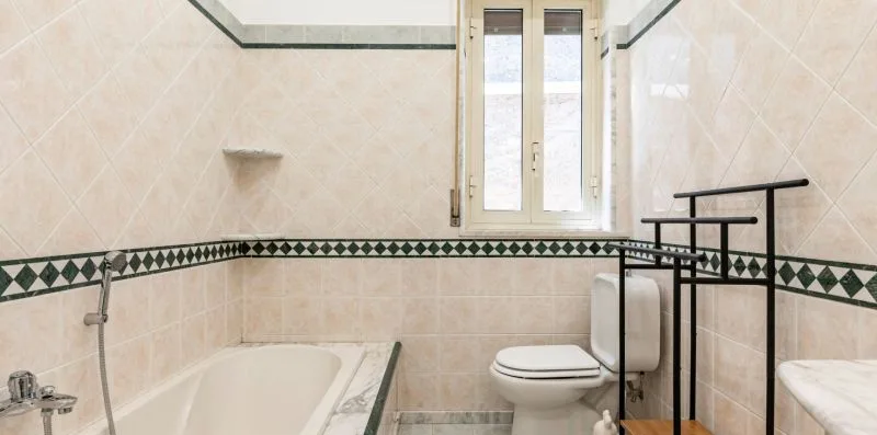 Un baño alicatado con bañera, inodoro y ventana.