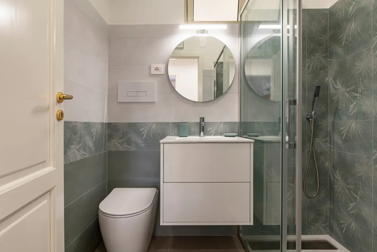 Un baño con lavabo, espejo redondo, inodoro y ducha de vidrio.