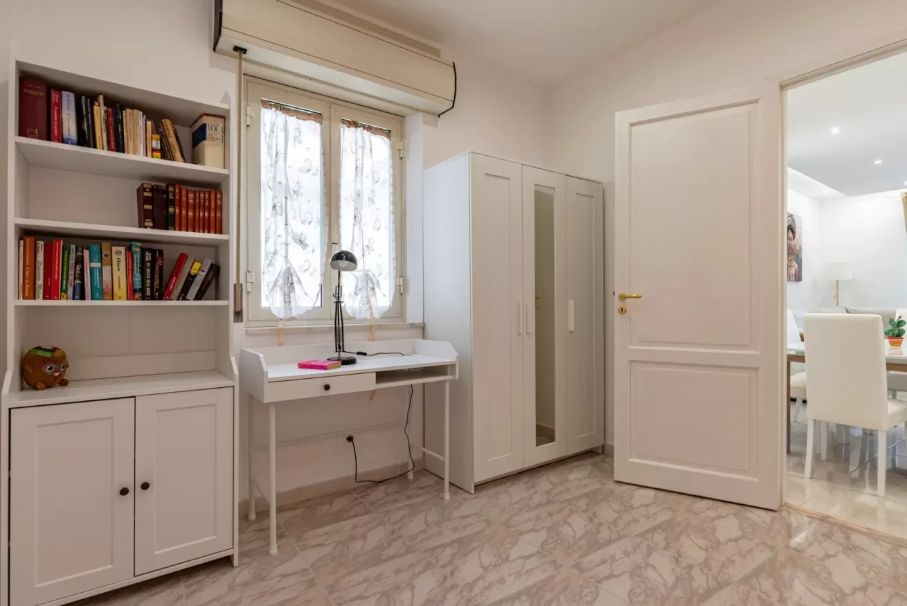 Una habitación luminosa con un escritorio bajo una ventana y estanterías empotradas.